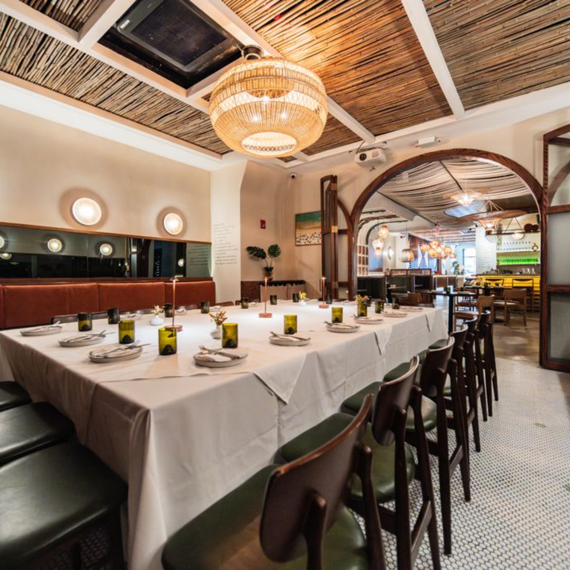 Elegant dining room with a large set table, woven chandelier, and wooden chairs with green cushions