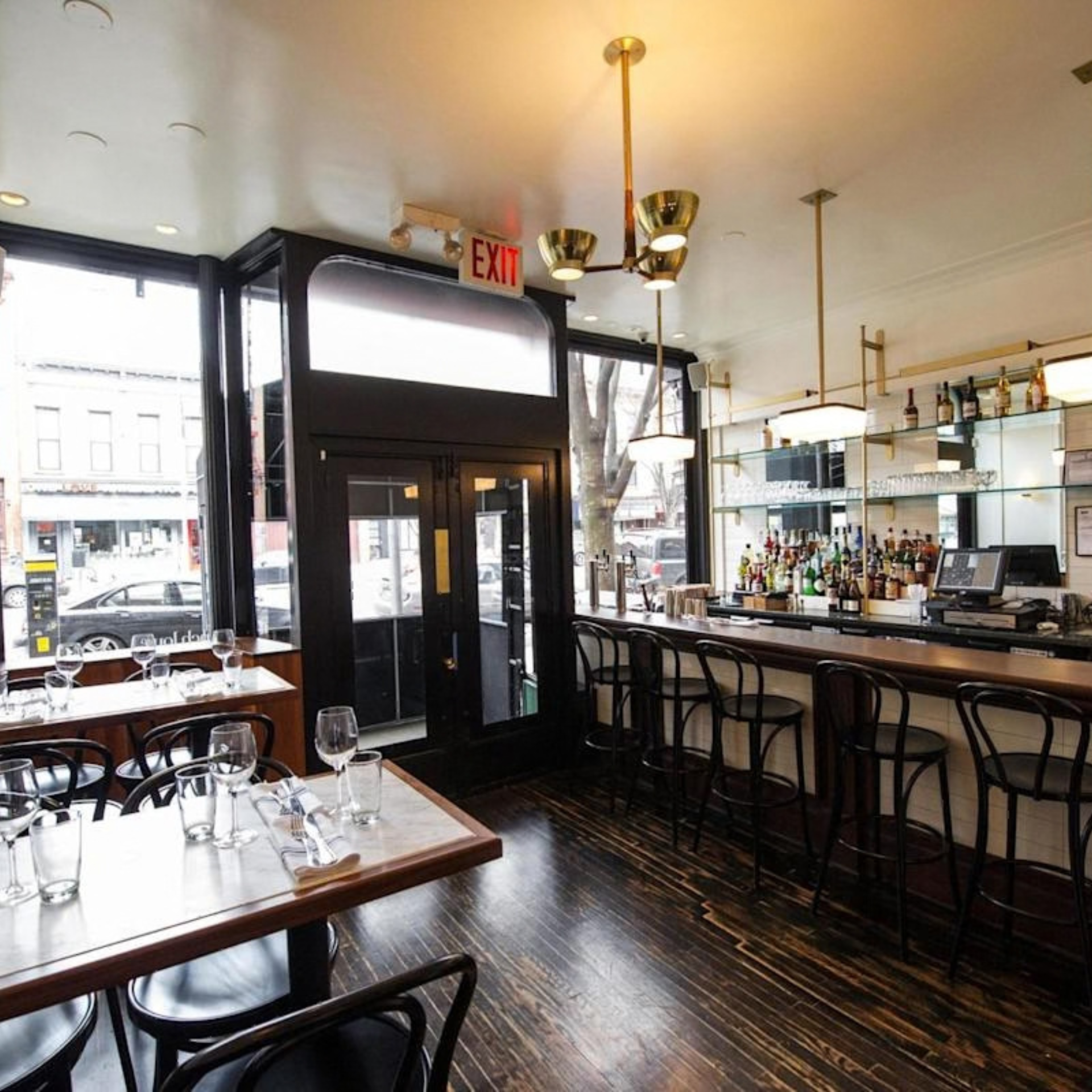 Modern restaurant interior with sleek bar, high stools, pendant lights, and large windows overlooking the street