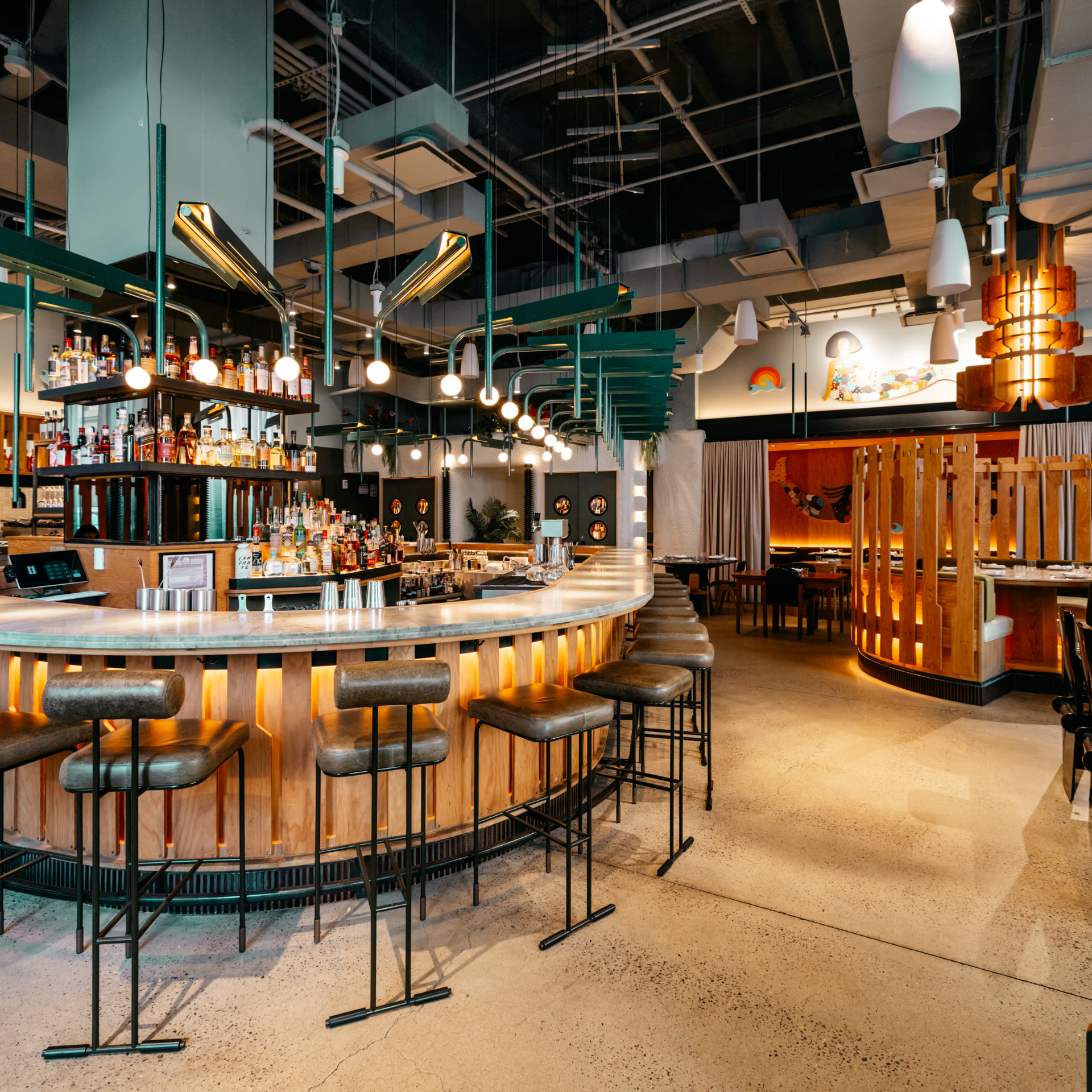 Modern bar with curved wooden counter, cushioned stools, and warm hanging lights in an upscale restaurant
