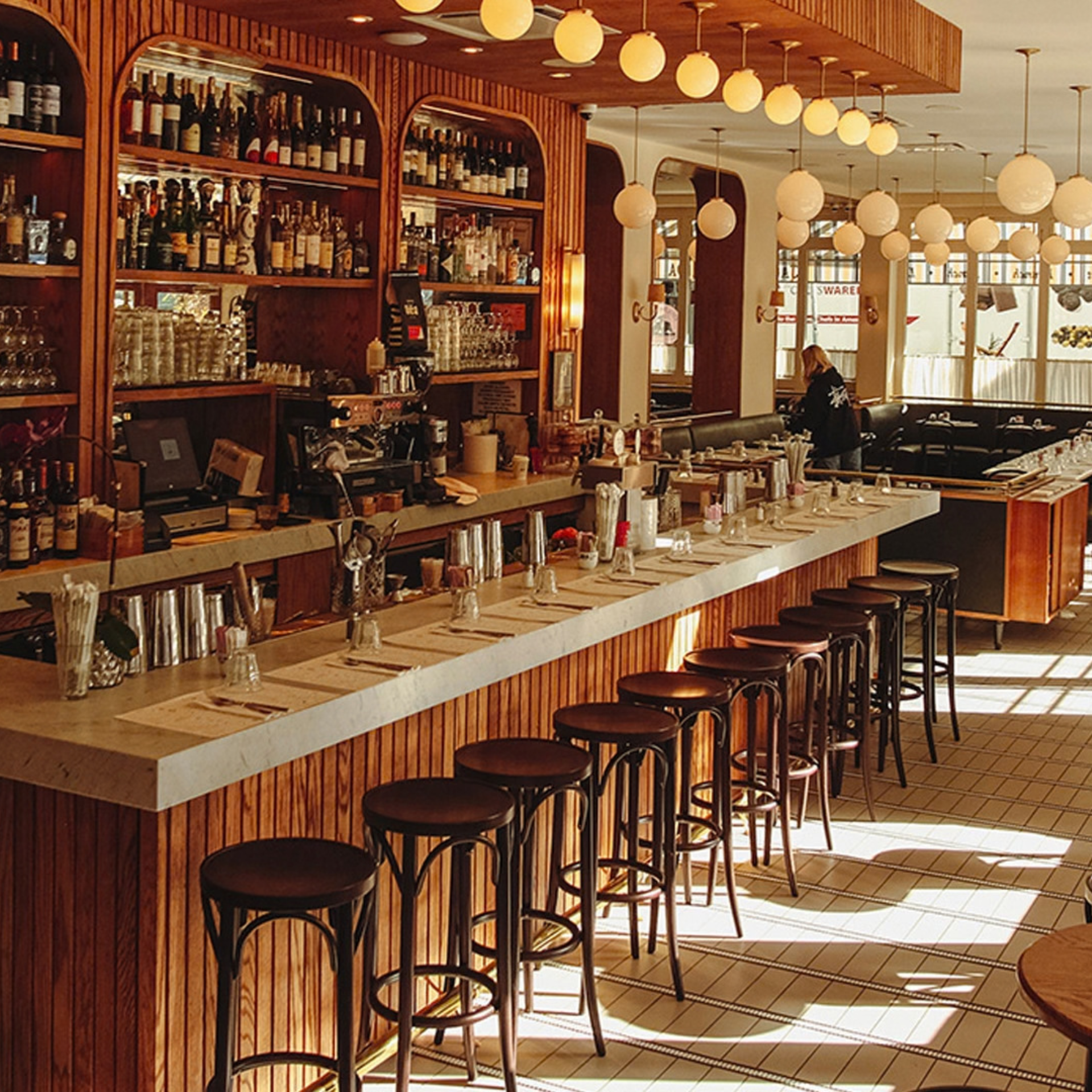 Stylish bar interior with marble counter, wooden stools, and shelves of bottles under warm pendant lights
