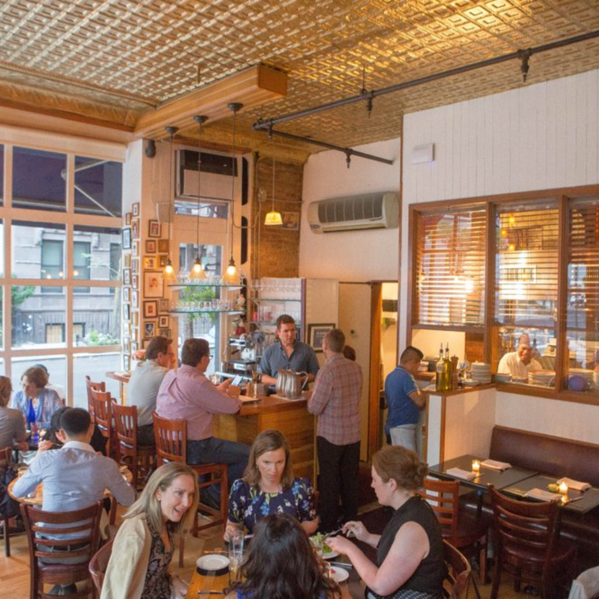 Cozy restaurant interior with golden tin ceiling, wooden furniture, bar seating, and patrons dining