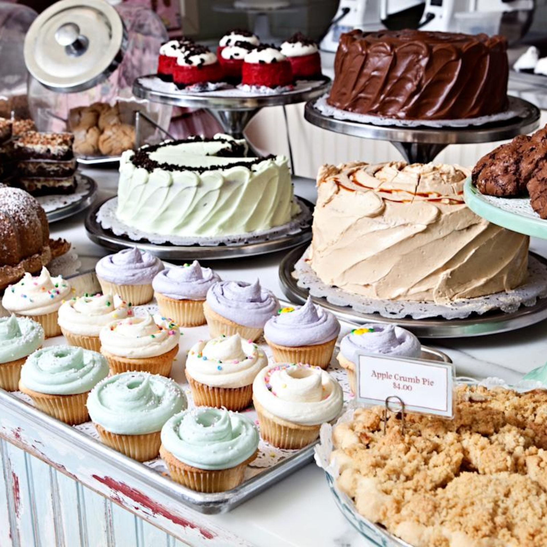Bakery display with cakes, pastel cupcakes, apple crumb pie, and assorted cookies