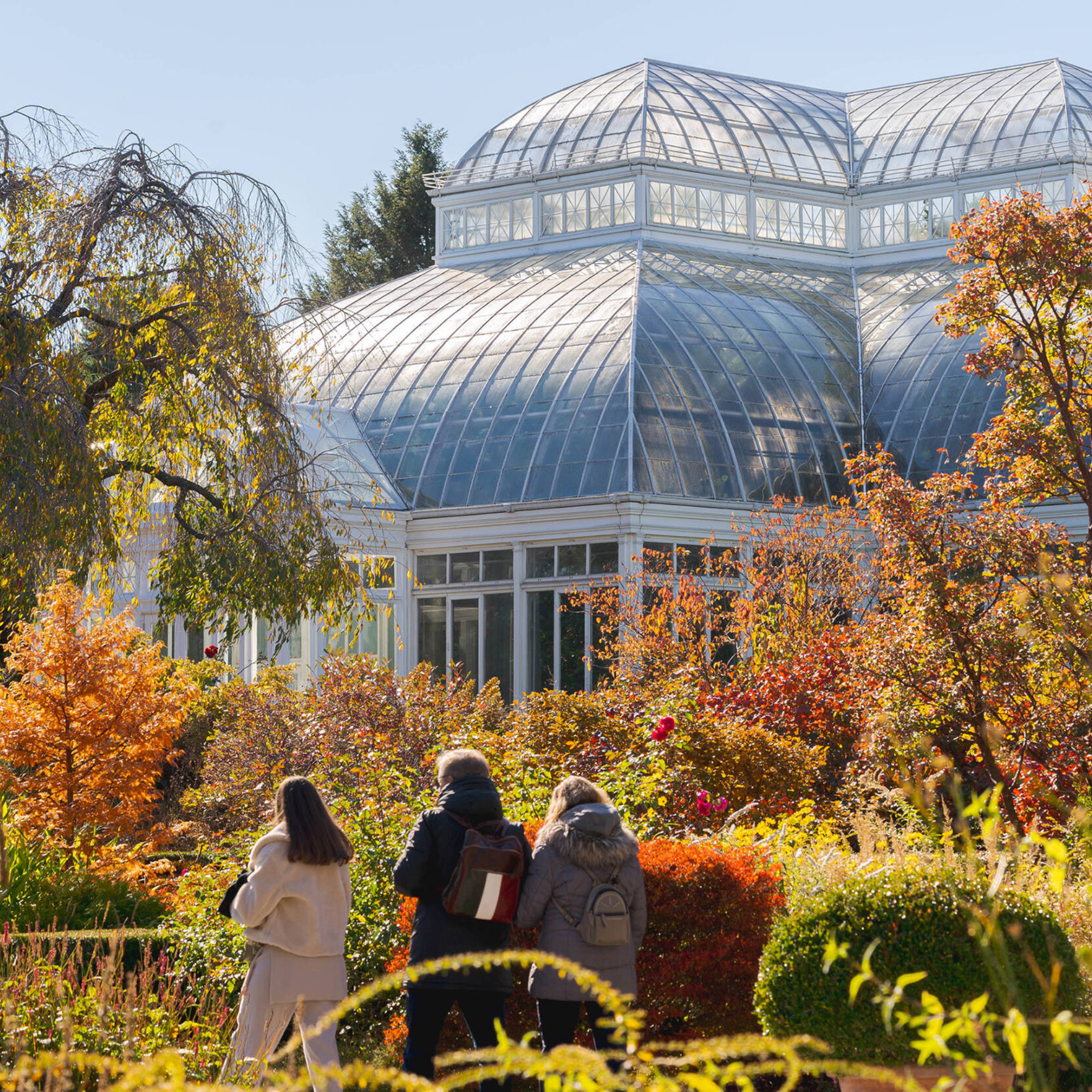 Glass-domed conservatory surrounded by autumn foliage with visitors walking along garden path