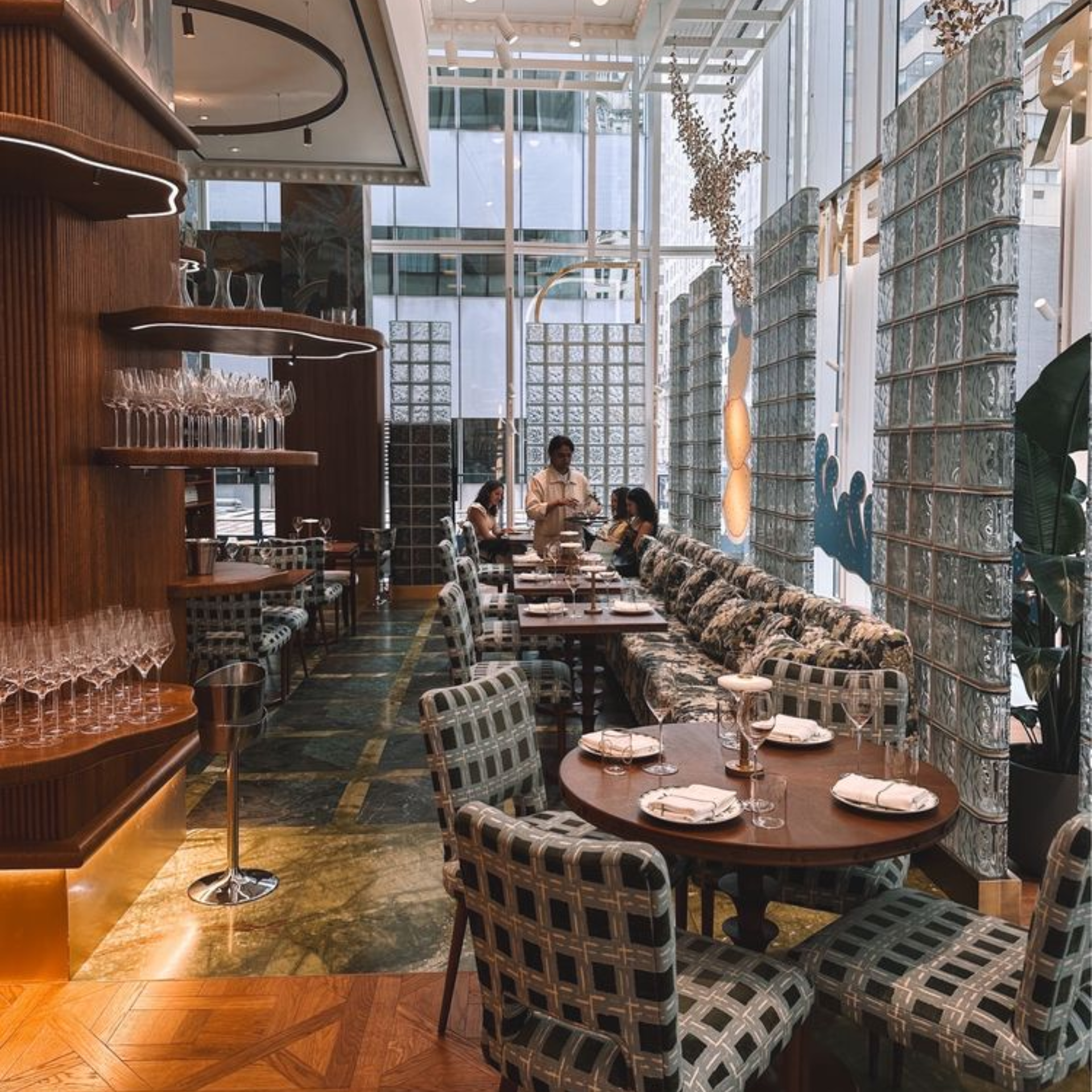 Upscale restaurant interior with patterned seating, marble accents, glass block wall, and guests dining