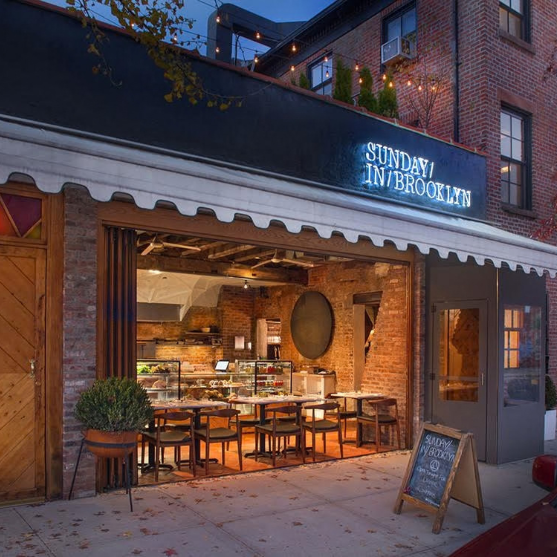 Exterior of Sunday in Brooklyn restaurant with exposed brick, warm lighting, and outdoor seating under neon signage