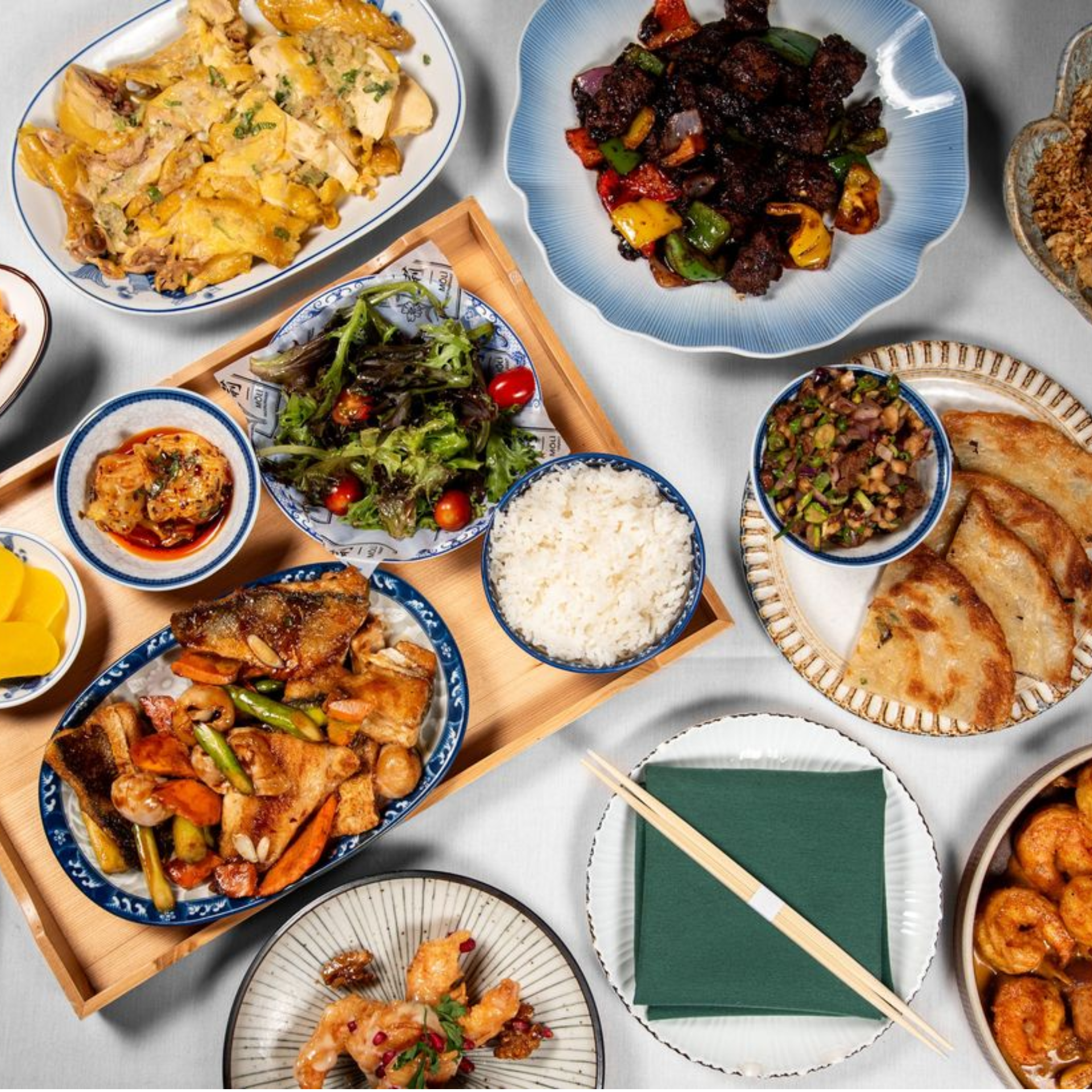 Table filled with assorted Chinese dishes including rice, stir‑fried meats, dumplings, salad, shrimp, and pickled vegetables