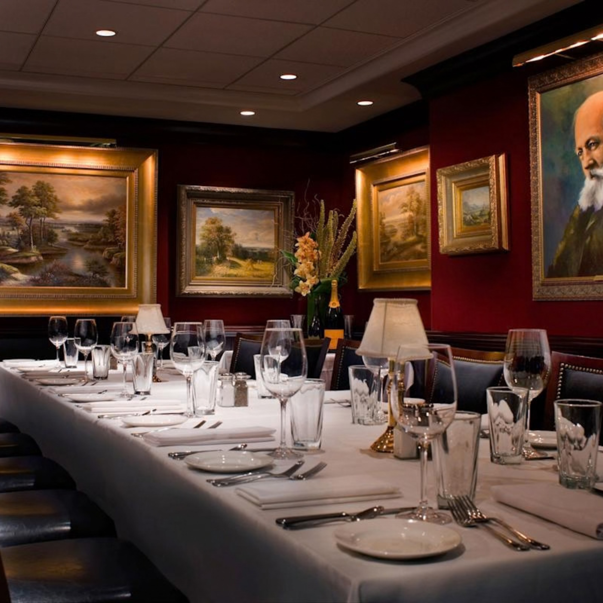 Elegant formal dining room with white tablecloths, wine glasses, and framed paintings on deep red walls