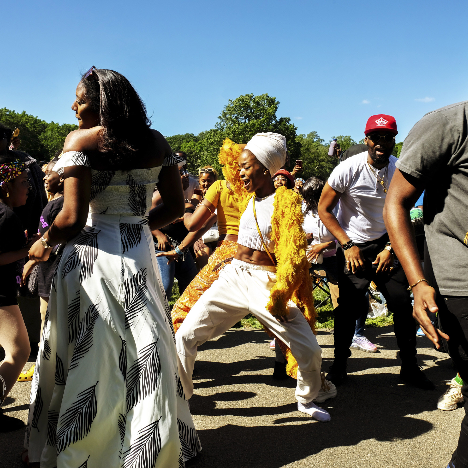 Outdoor cultural festival in park with diverse crowd dancing, colorful outfits, joyful community celebration under sunny sky