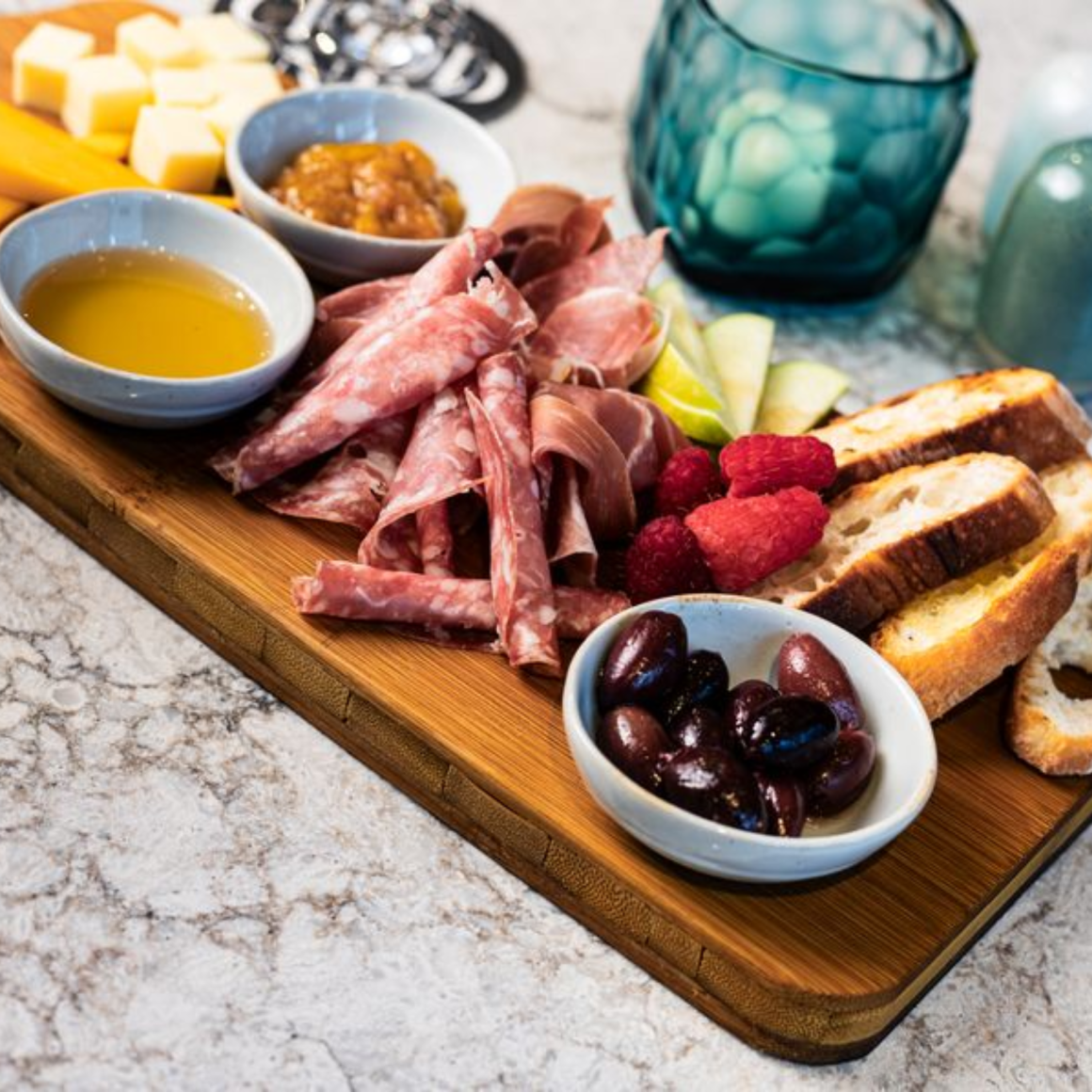 Charcuterie board with cured meats, cheeses, bread, fruit, olives, and dips on marble countertop