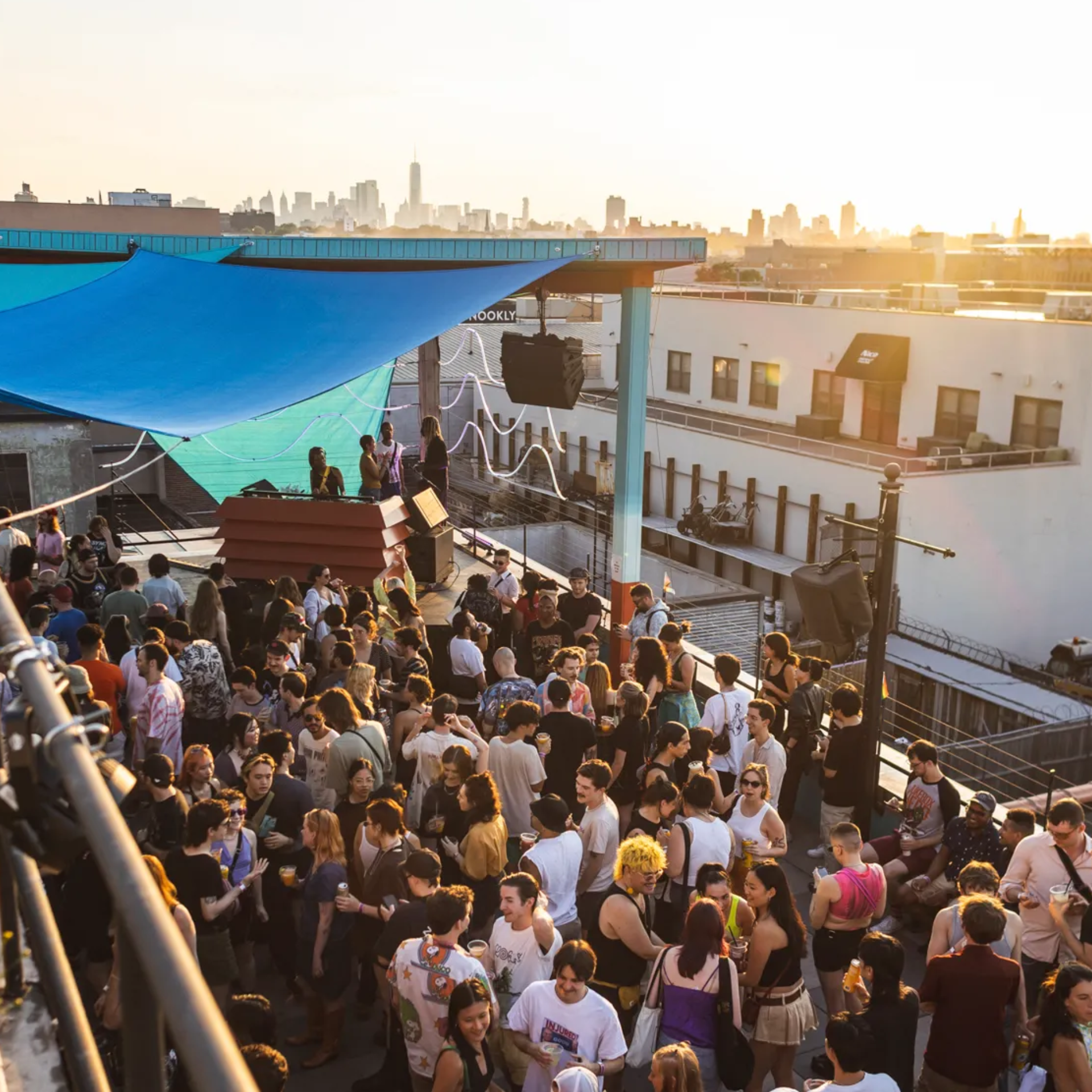Sunset rooftop party with DJ booth, crowd socializing, city skyline view, and golden hour atmosphere