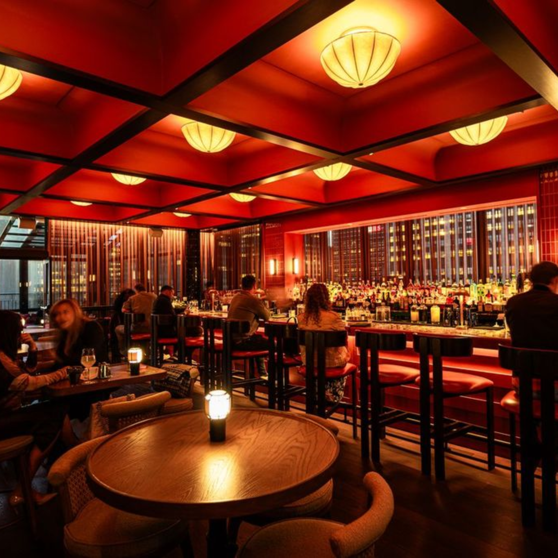 Upscale NYC bar interior with warm red lighting, geometric ceiling panels, and city views, intimate nightlife destination for cocktails, socializing, and daily things to do in NYC any day