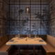 Cozy restaurant booth with wooden table, cushioned seating, warm pendant light, and artistic wall of circular patterns and shadows