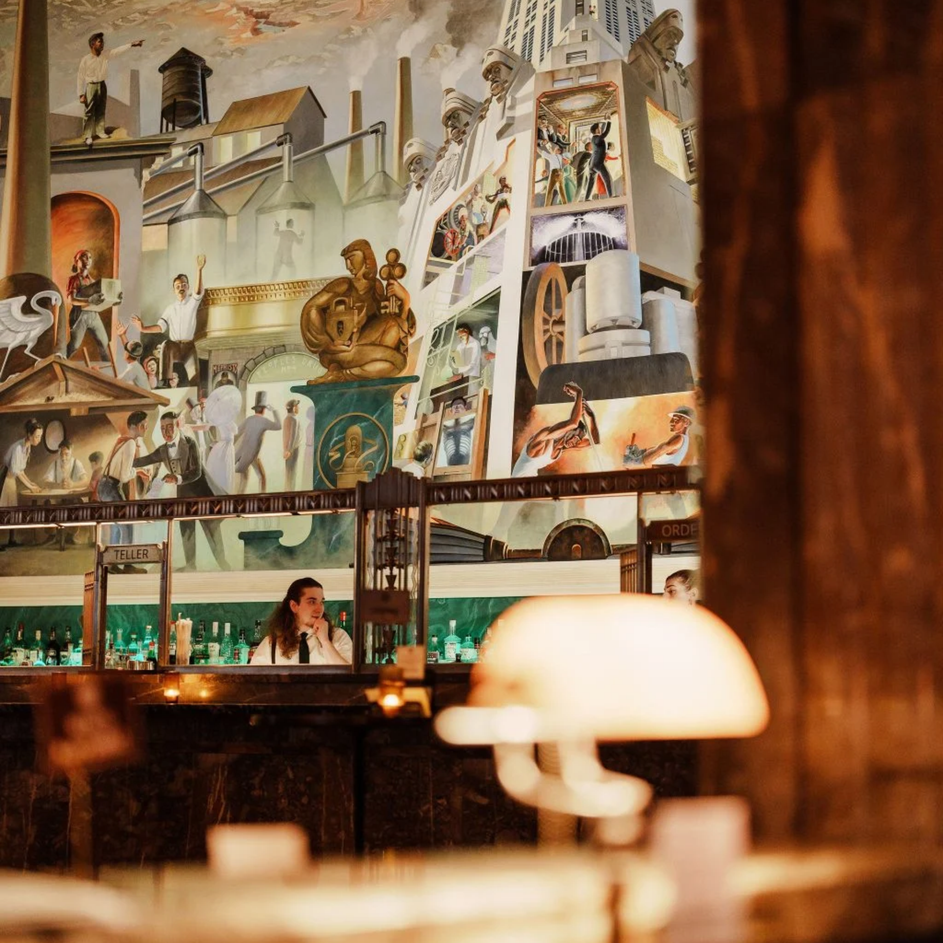 Bar with large industrial mural and bartender at counter