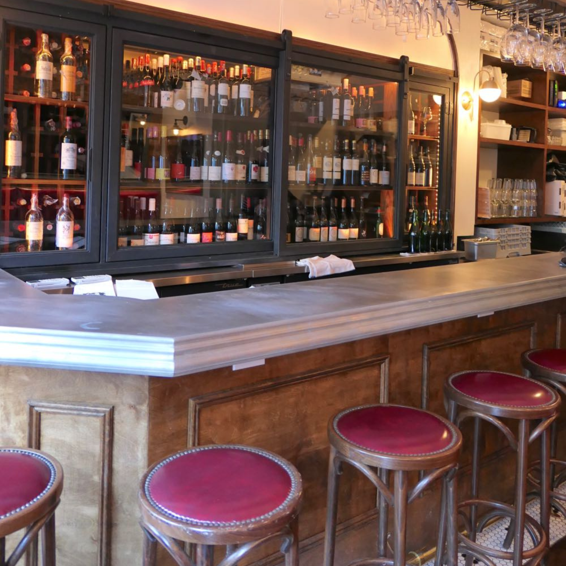 Wine bar with wood counter, red-cushioned stools, glass racks, and warm lighting for a cozy, vintage-inspired atmosphere