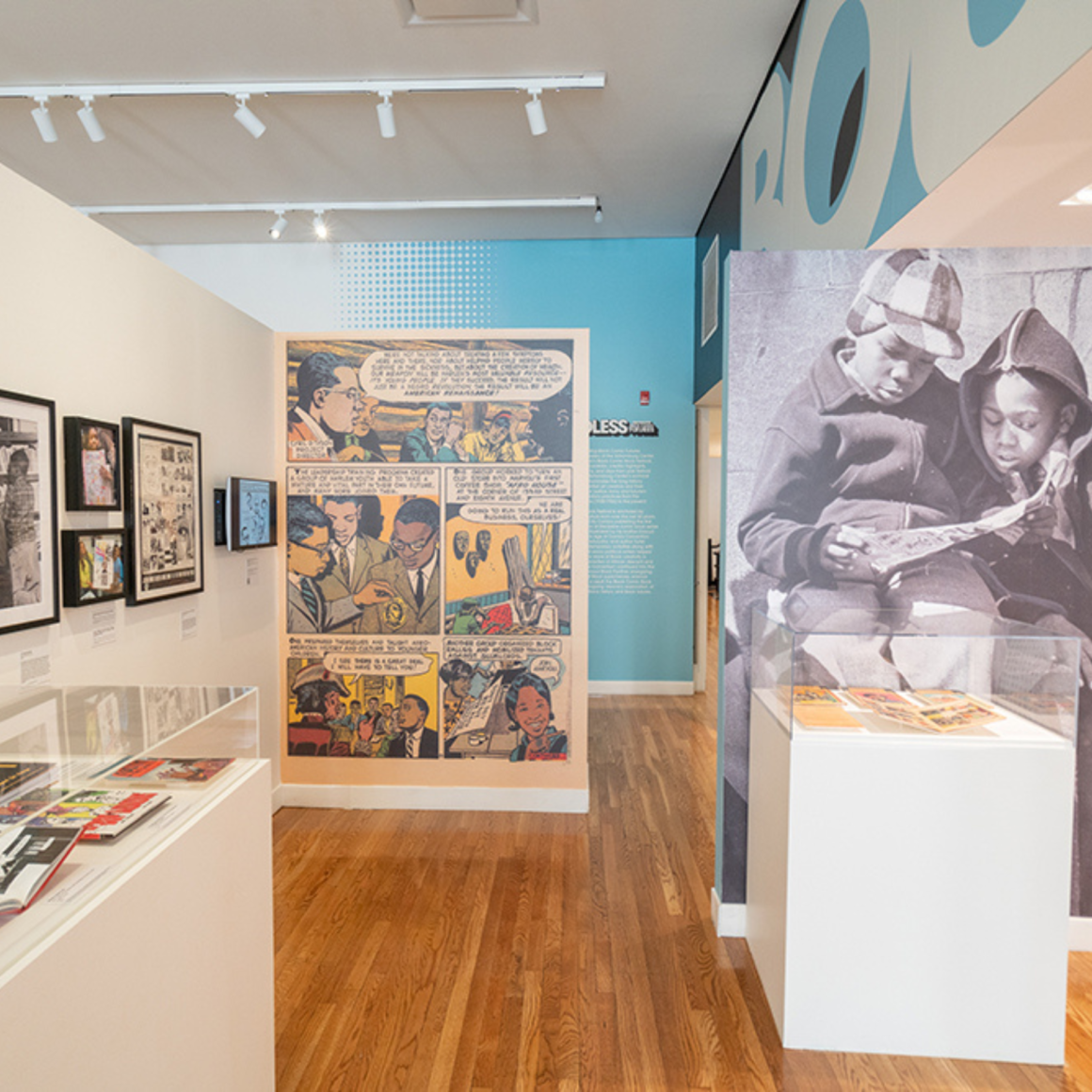 Comic art exhibit with mural, framed pages, and photo of children reading