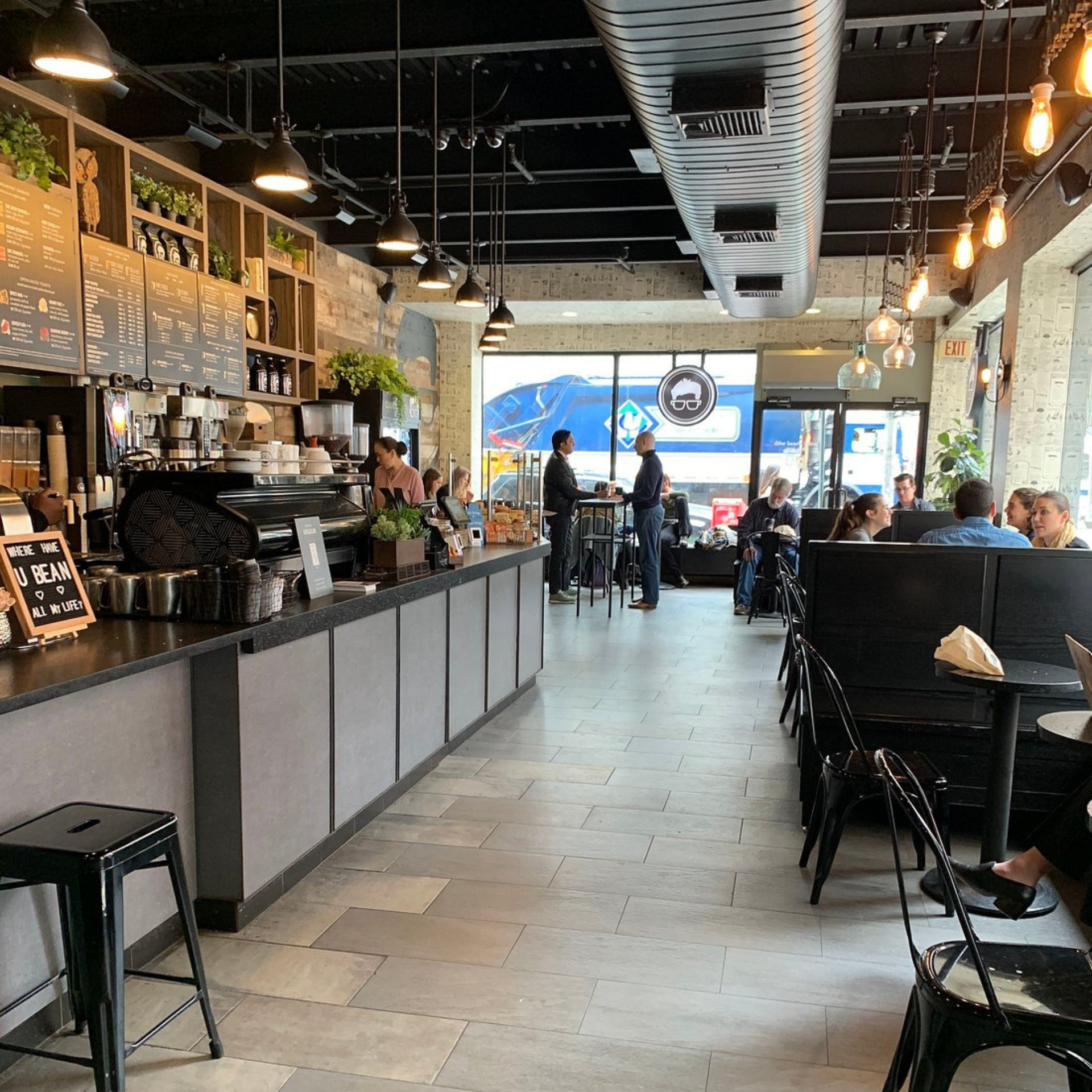 Modern café interior with baristas at counter, menu board, cozy seating, hanging lights, and natural light from windows