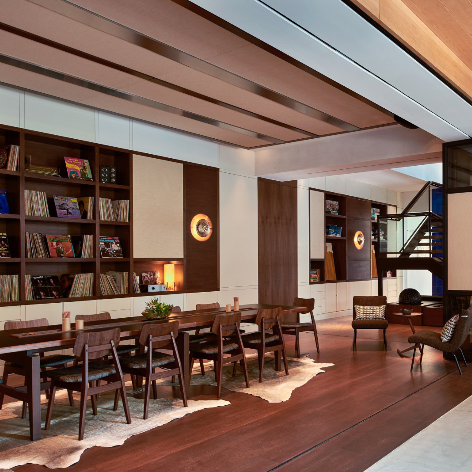 Modern dining and lounge space with a long wooden table, cowhide rug, and shelves filled with vinyl records and books
