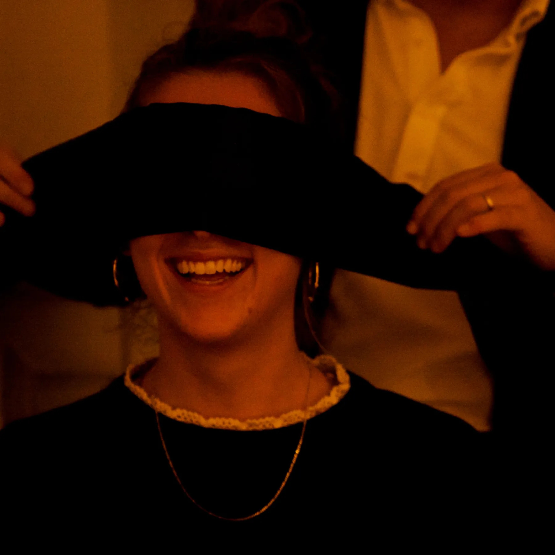 Smiling person being blindfolded in warmly lit setting