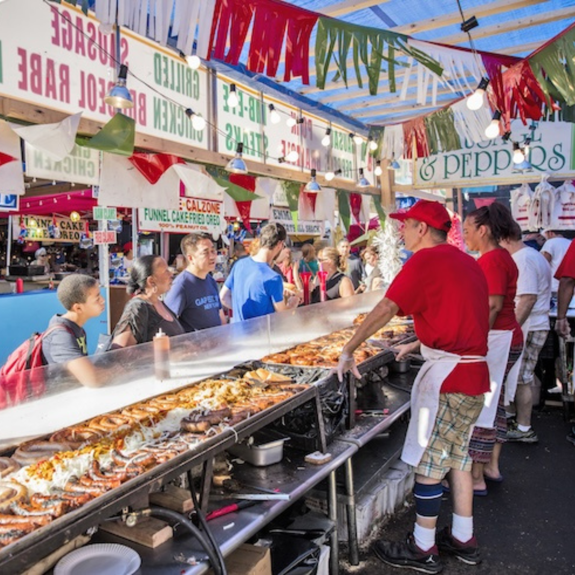 Seafood vendor in red shirt serves steaming lobsters and crabs at festive market stall, surrounded by signs, streamers, and crowd