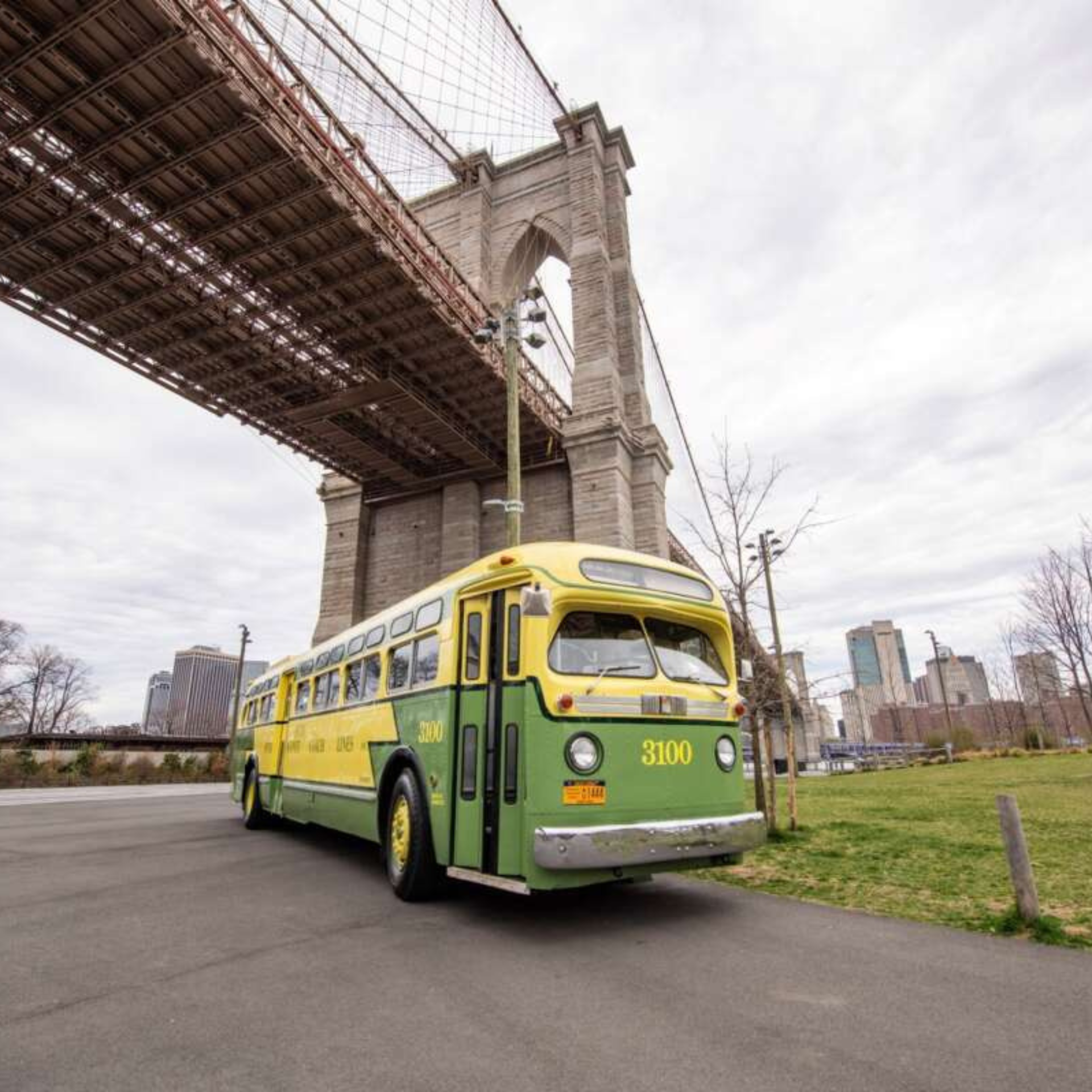 Vintage green and yellow bus near Brooklyn Bridge in NYC with park and city skyline