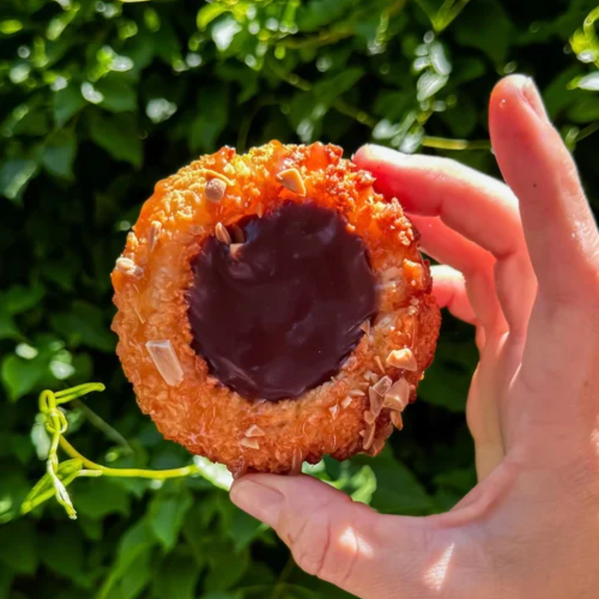 Hand holding round pastry with chocolate center and almond flakes