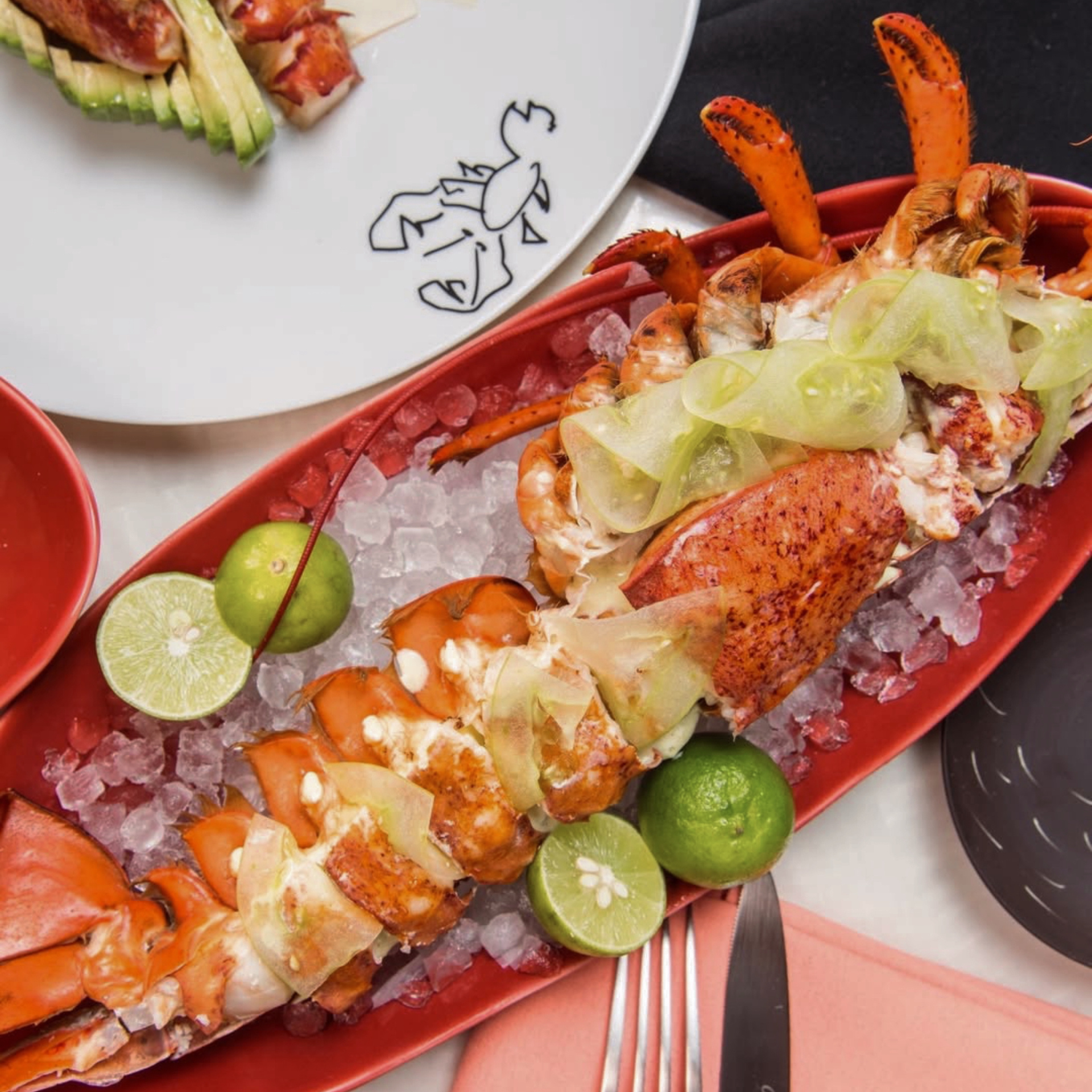 Lobster on ice with cucumber slices and limes in red dish