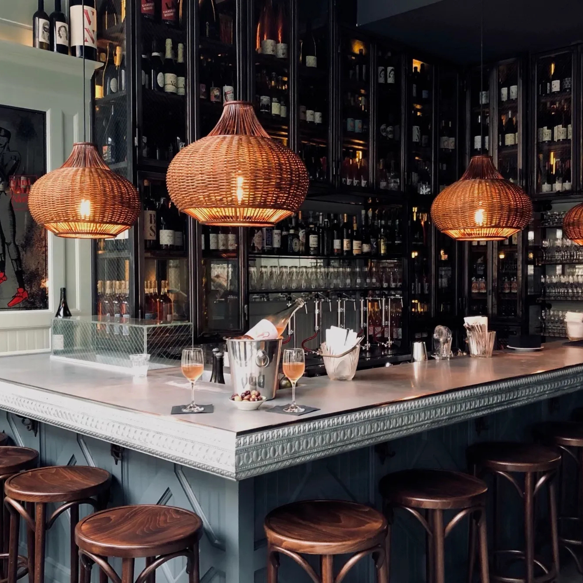 Bar with ornate counter, rattan pendant lights, wine glasses, and cozy setup featuring rosé, snacks, and warm ambiance