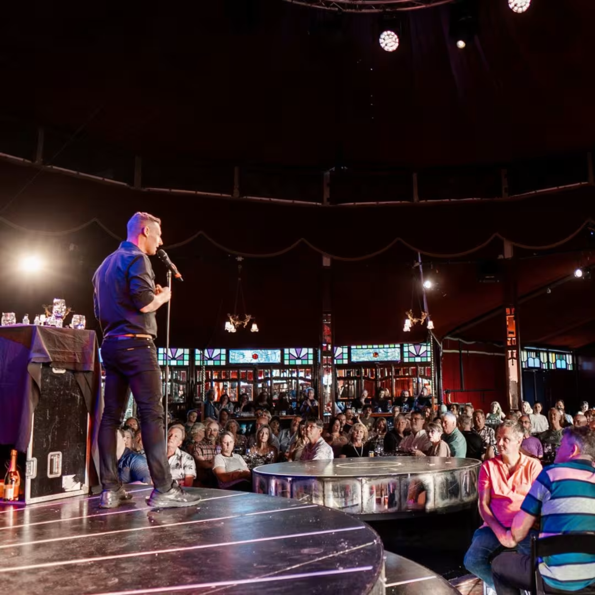 Performer with microphone on circular stage before seated audience