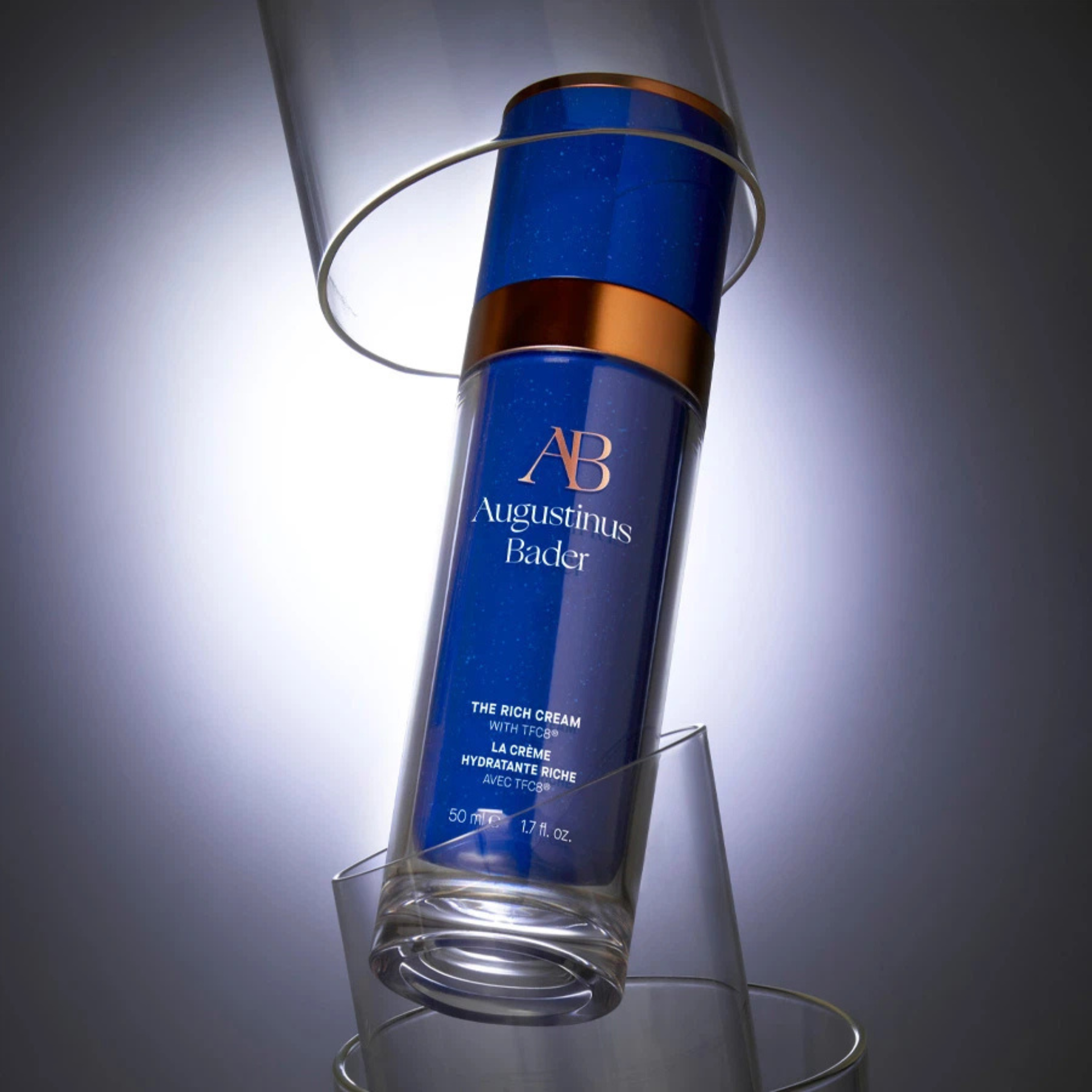 Luxury skincare spotlight: Augustinus Bader’s blue bottle of The Rich Cream glows between glass cylinders in dramatic light