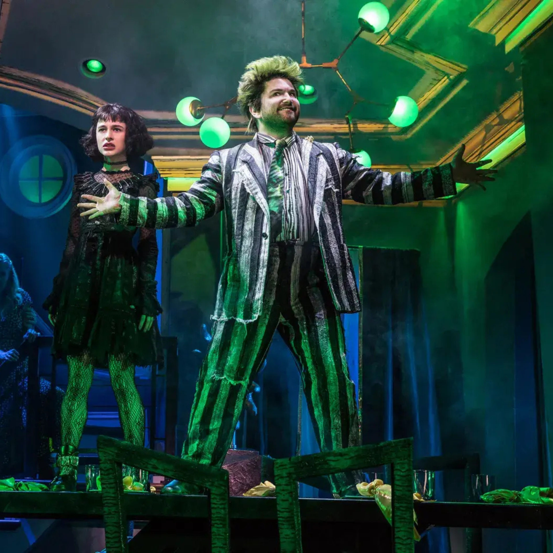 Beetlejuice musical scene with striped-suit actor on table and green-lit stage, capturing spooky humor and dramatic flair