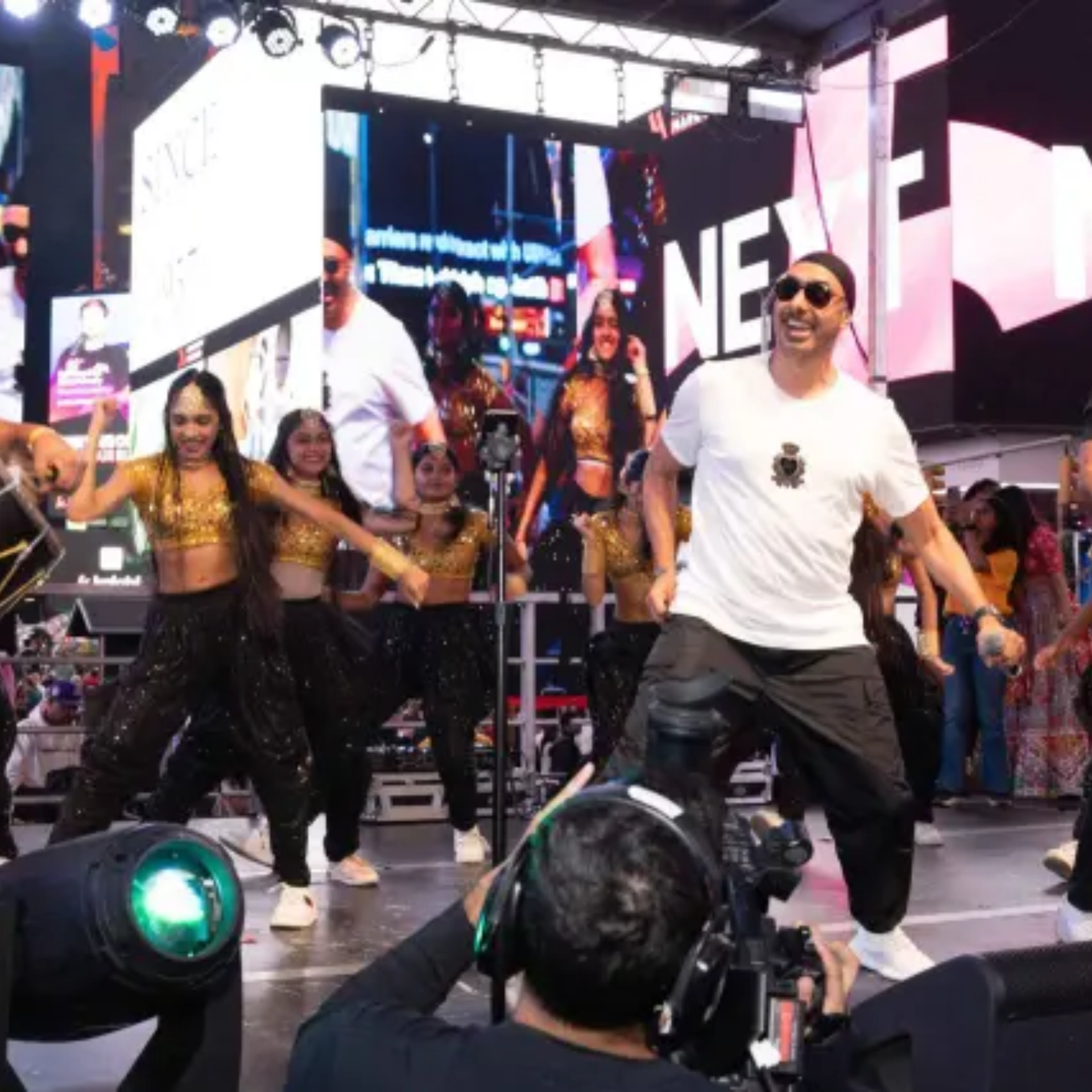 Singer with dancers on lit stage before large screen