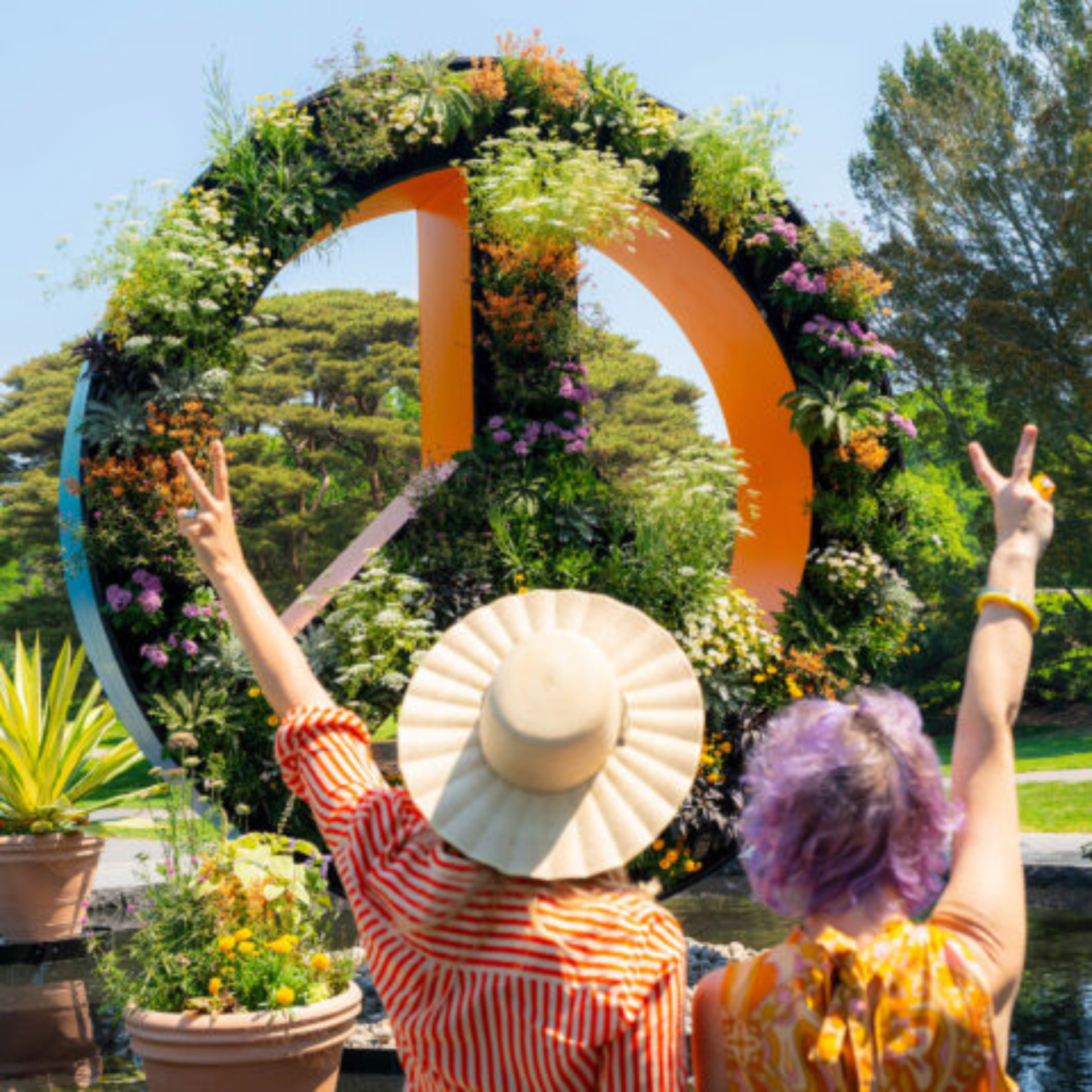 Two people making peace signs by floral peace sculpture