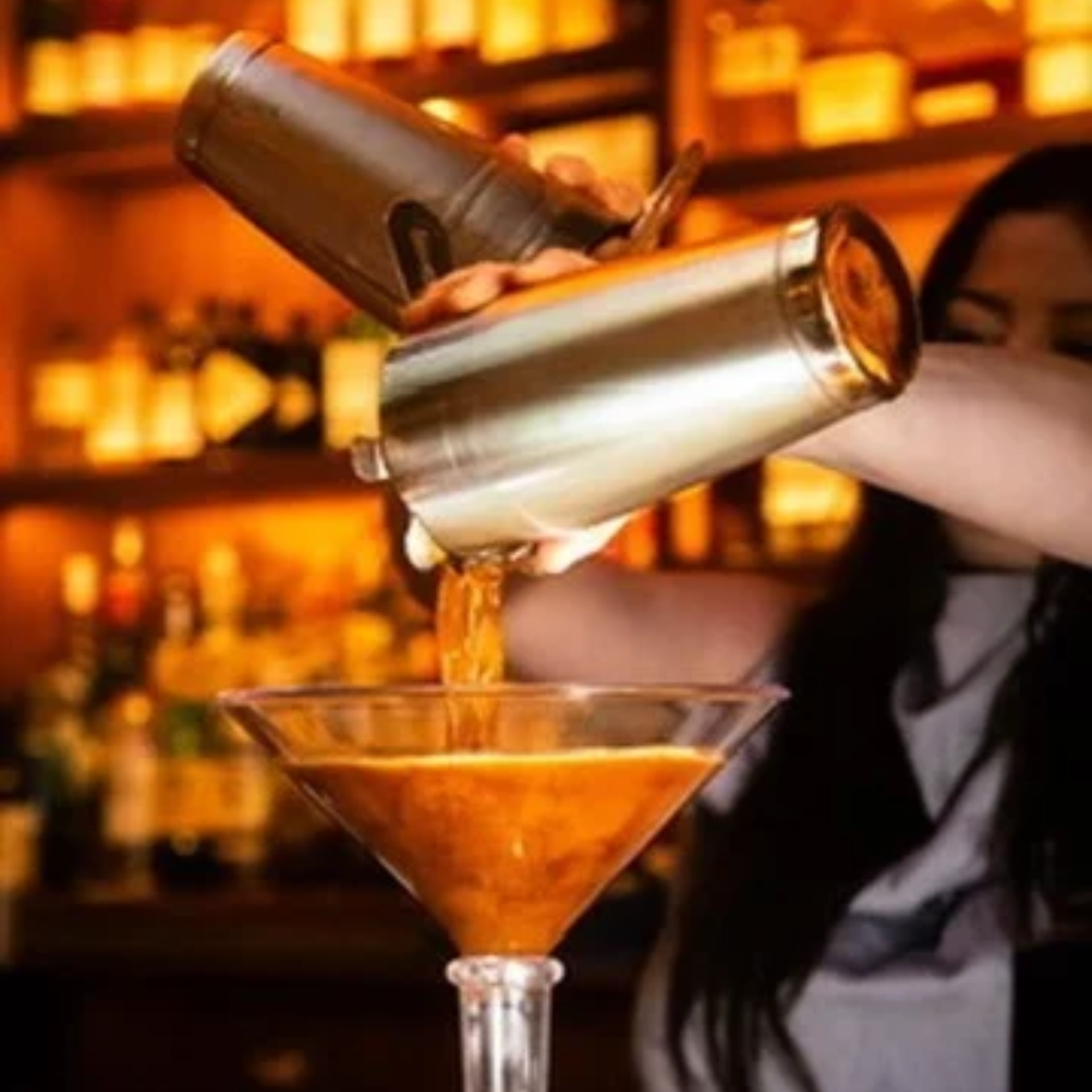 Bartender pouring amber cocktail into martini glass