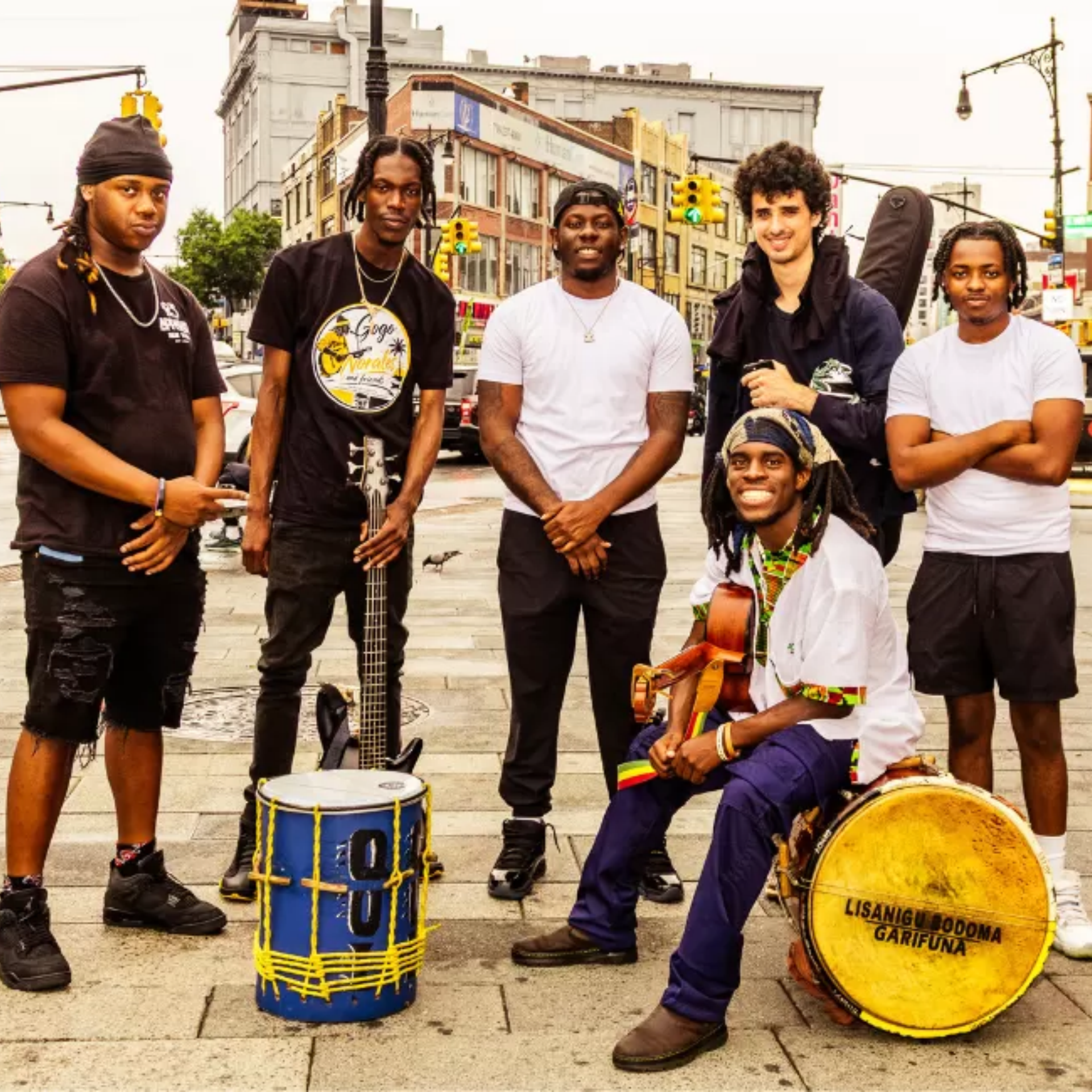 Six musicians with guitars and drums posing on city street