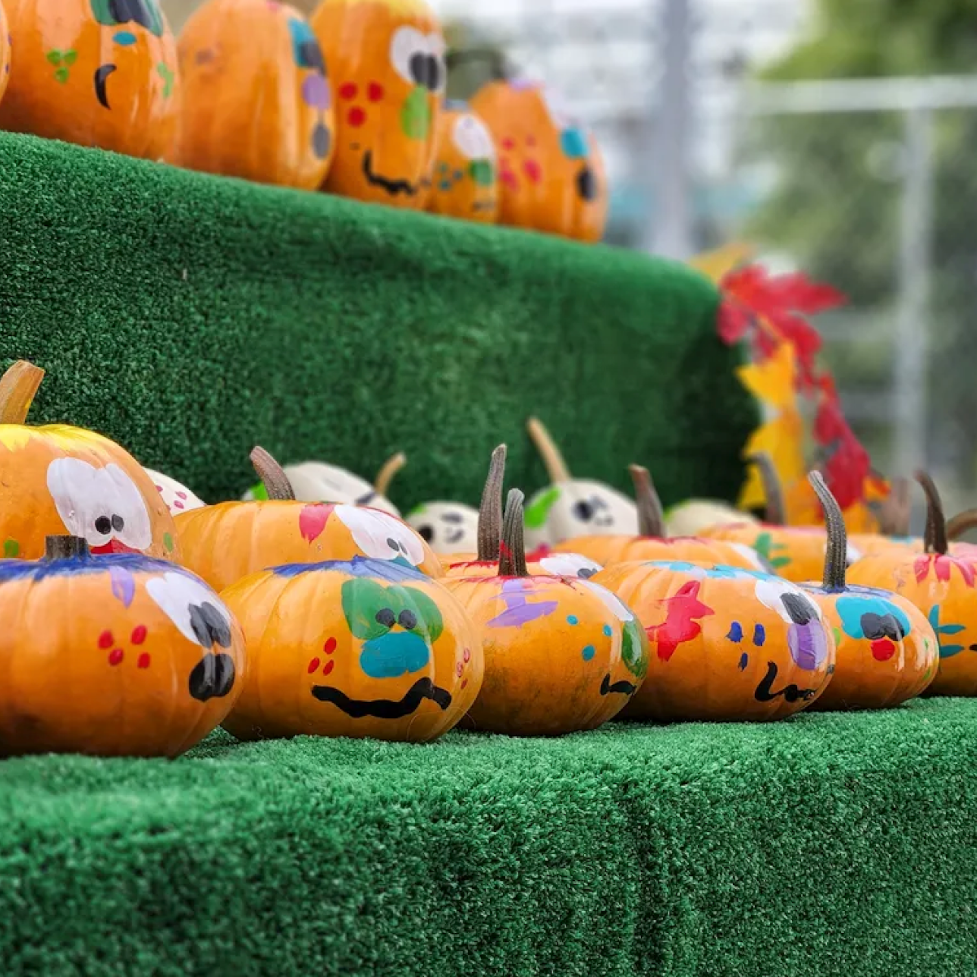 Whimsically painted pumpkins with colorful faces sit on green steps in a cheerful autumn-themed display
