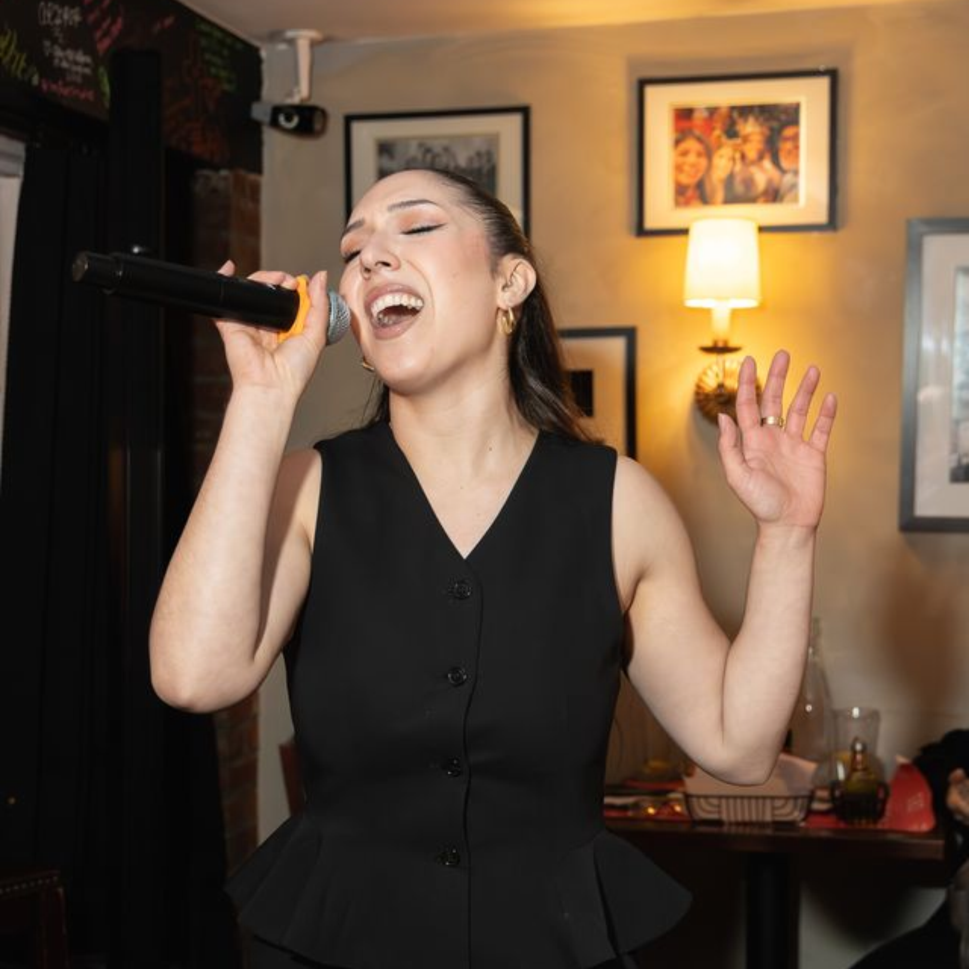 Singer in a black dress performing in a warmly lit, decorated room