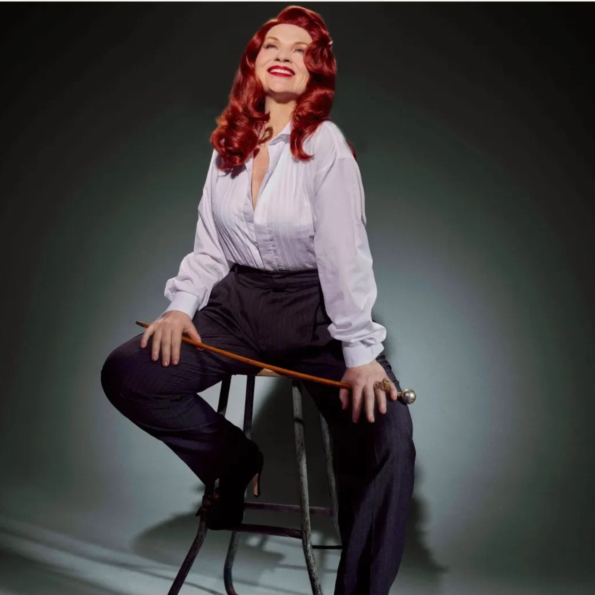 Person with red hair on stool holding cane in vintage‑style portrait