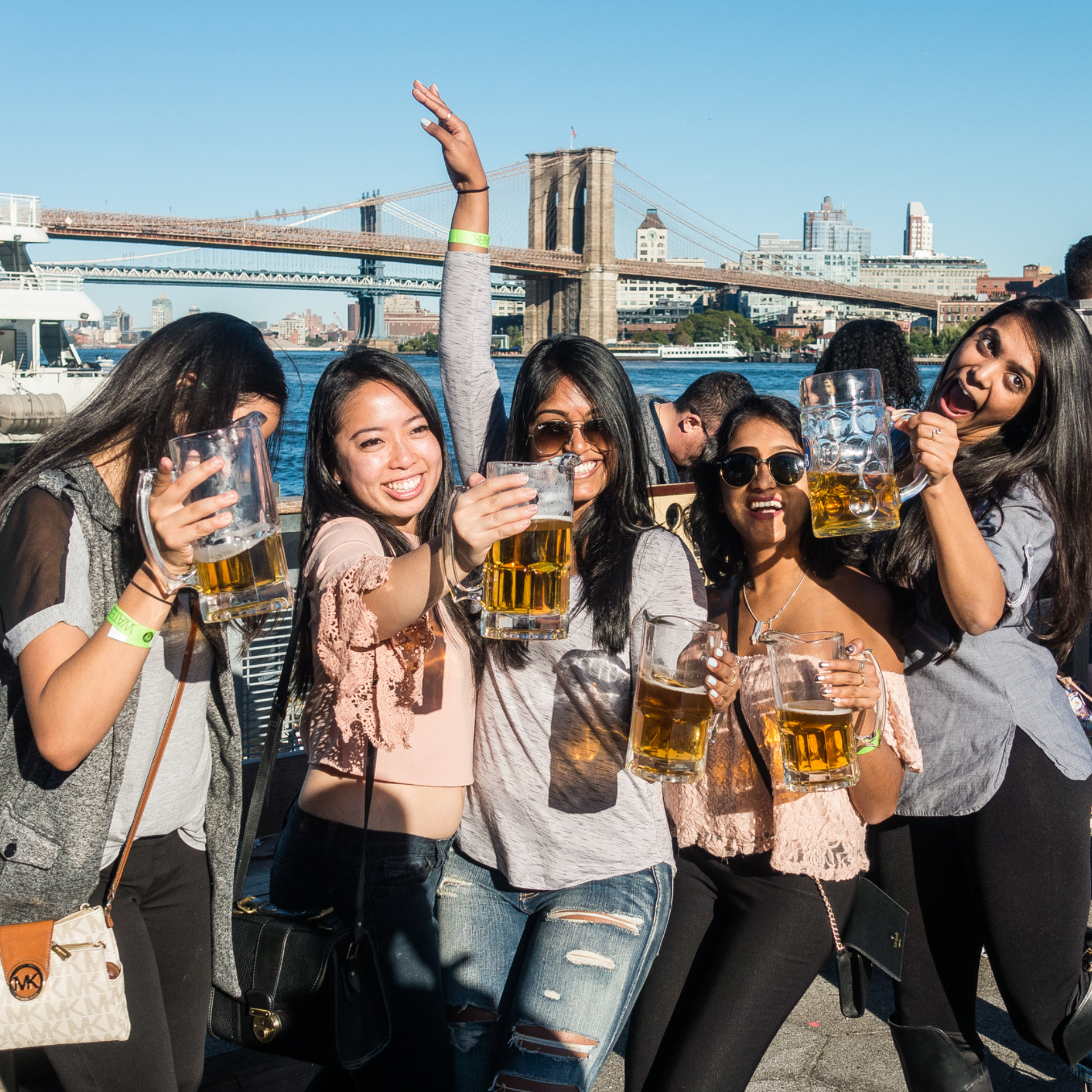 Group holding beer mugs by Brooklyn Bridge waterfront