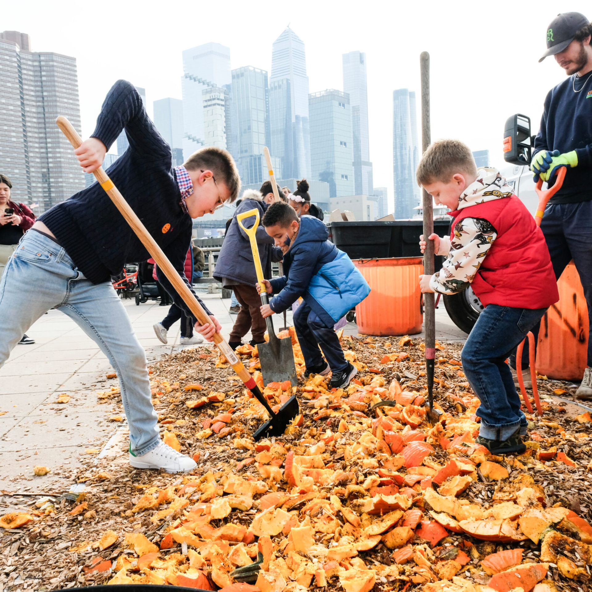 Children use shovels and rakes to smash and spread pumpkin pieces during a city-based outdoor activity