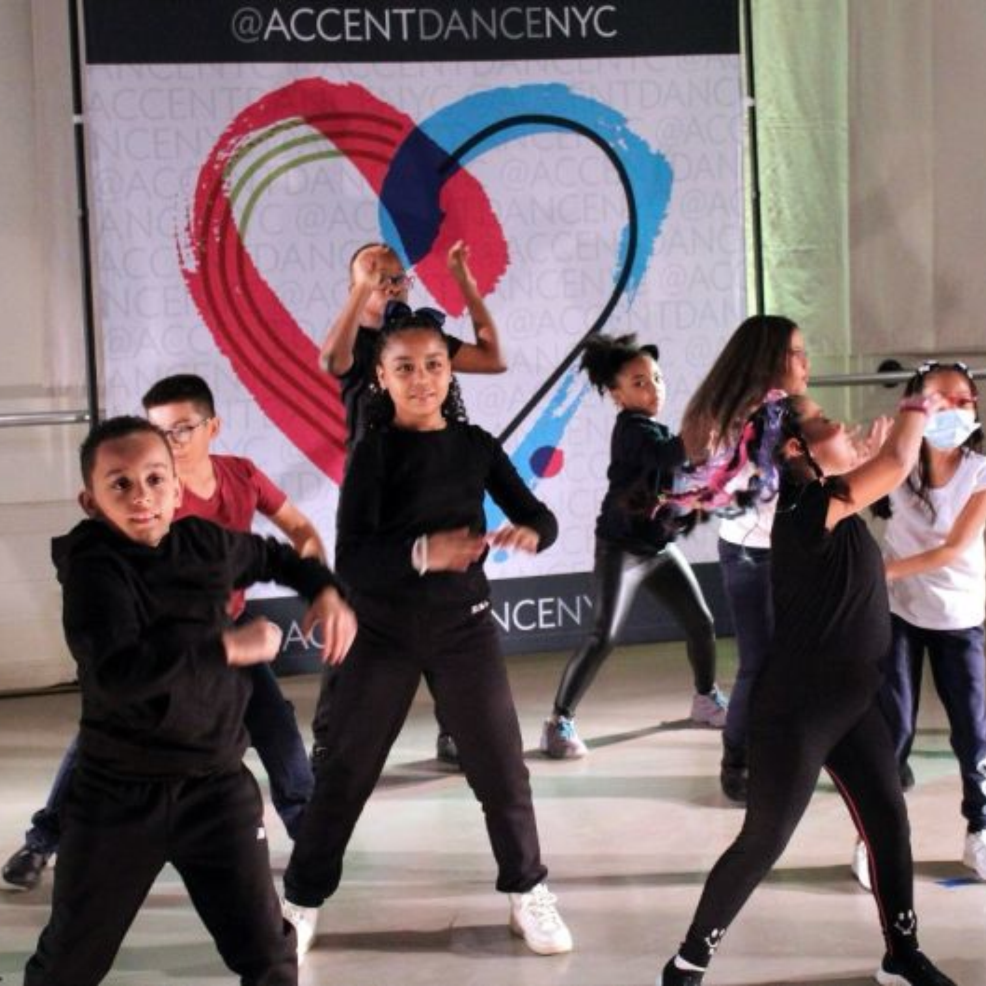 Kids dancing before colorful heart backdrop with Accent Dance NYC text
