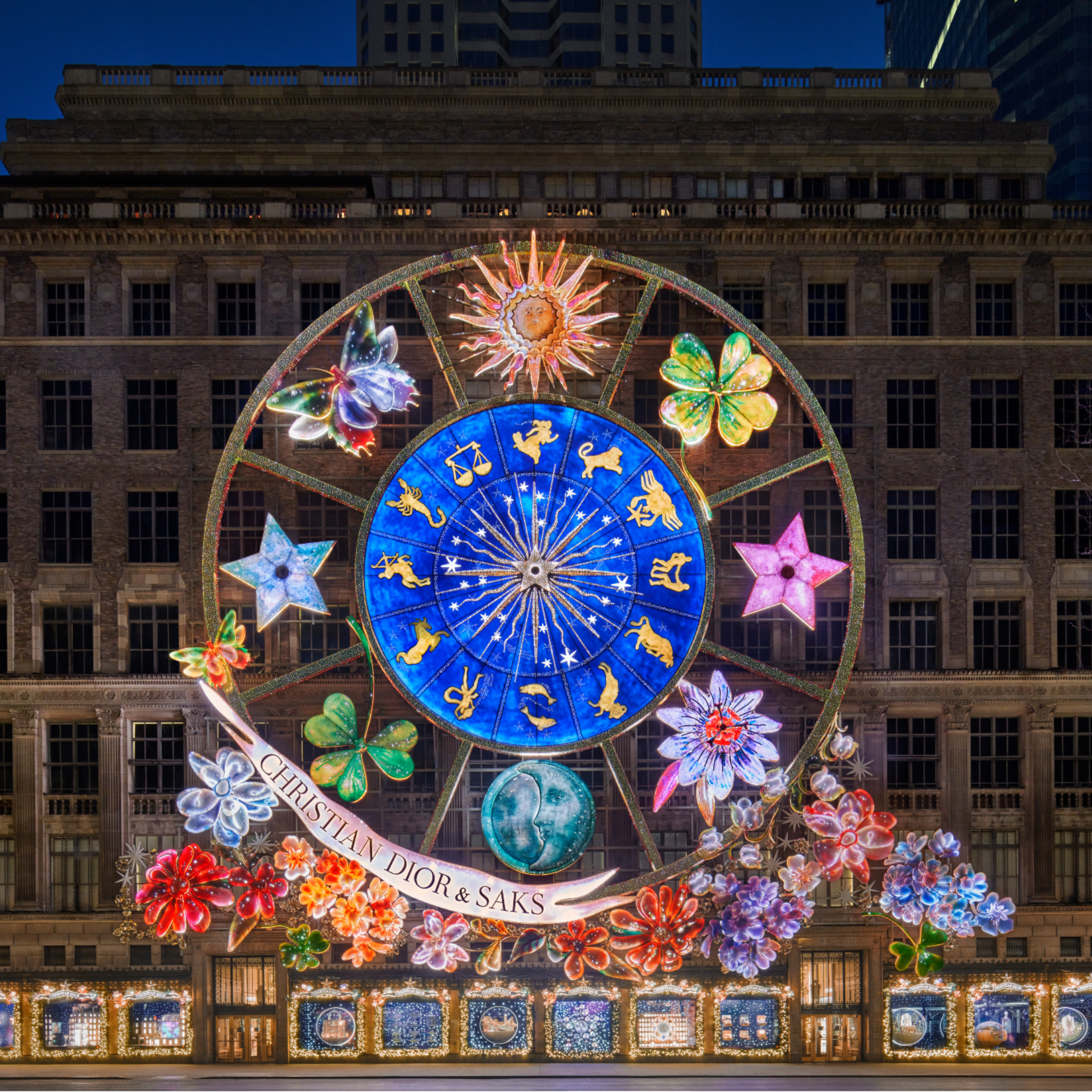 Festive zodiac-themed holiday display lights up the Saks Fifth Avenue facade in NYC, featuring astrological symbols, celestial decorations, and a banner for Christian Dior & Saks