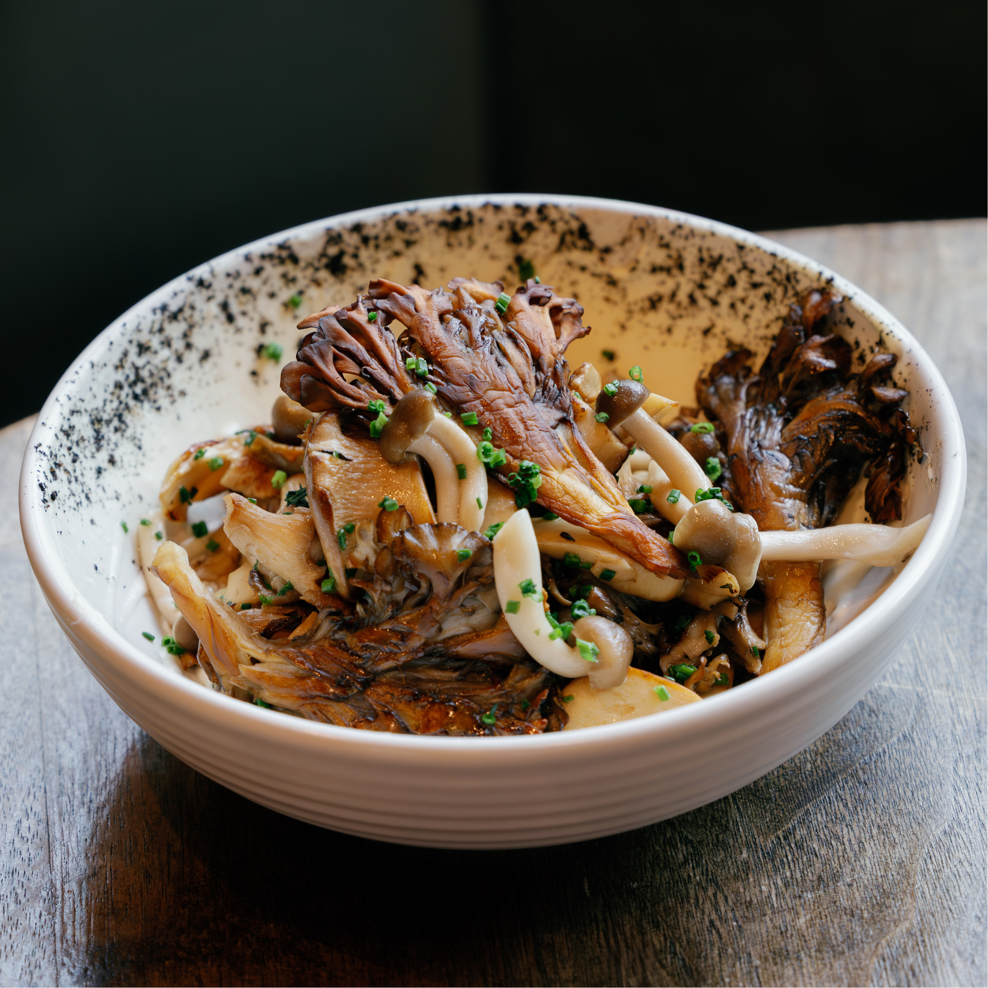 Bowl of assorted cooked mushrooms garnished with chives, served in a white bowl with a speckled black interior