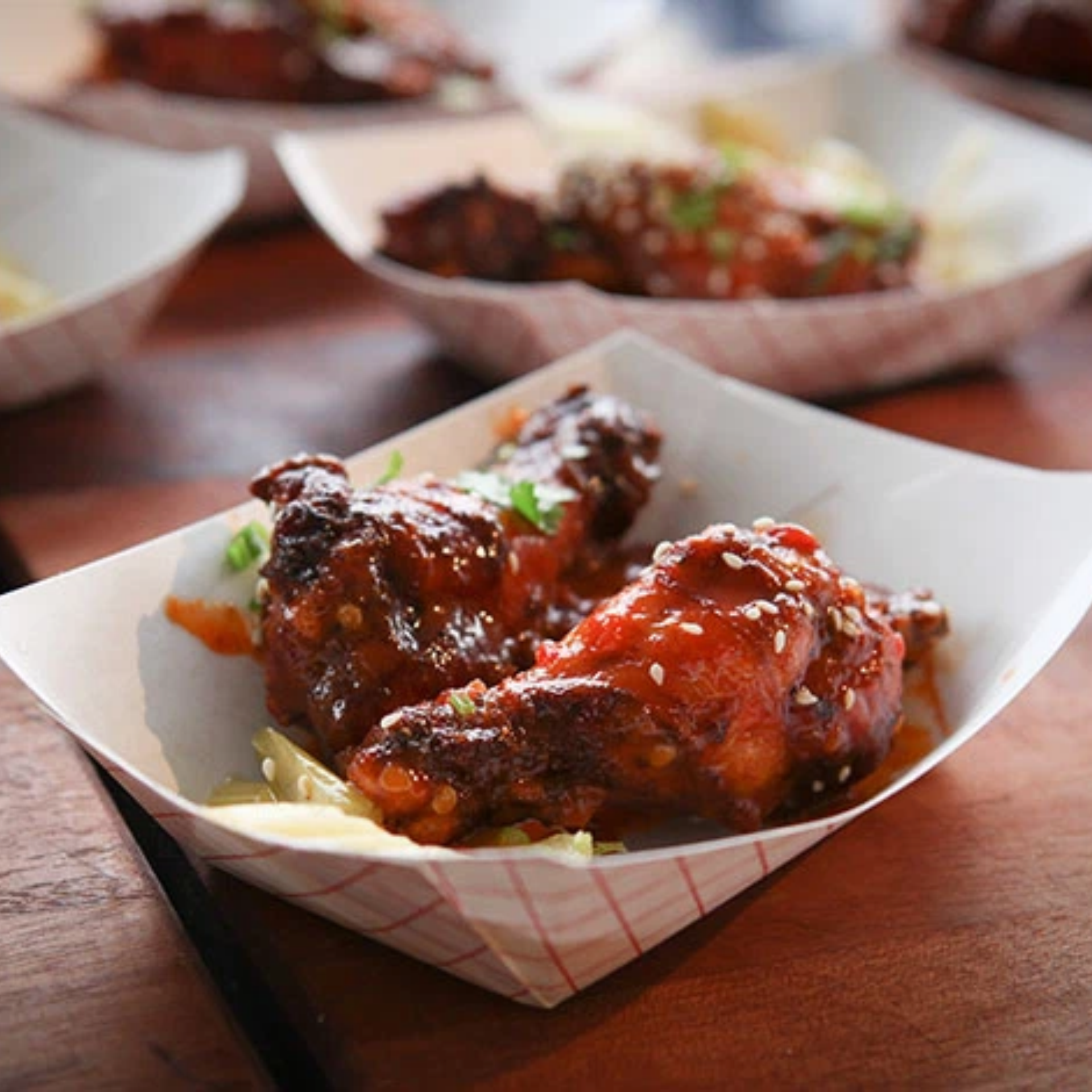 Paper tray with glazed chicken wings topped with sesame and herbs