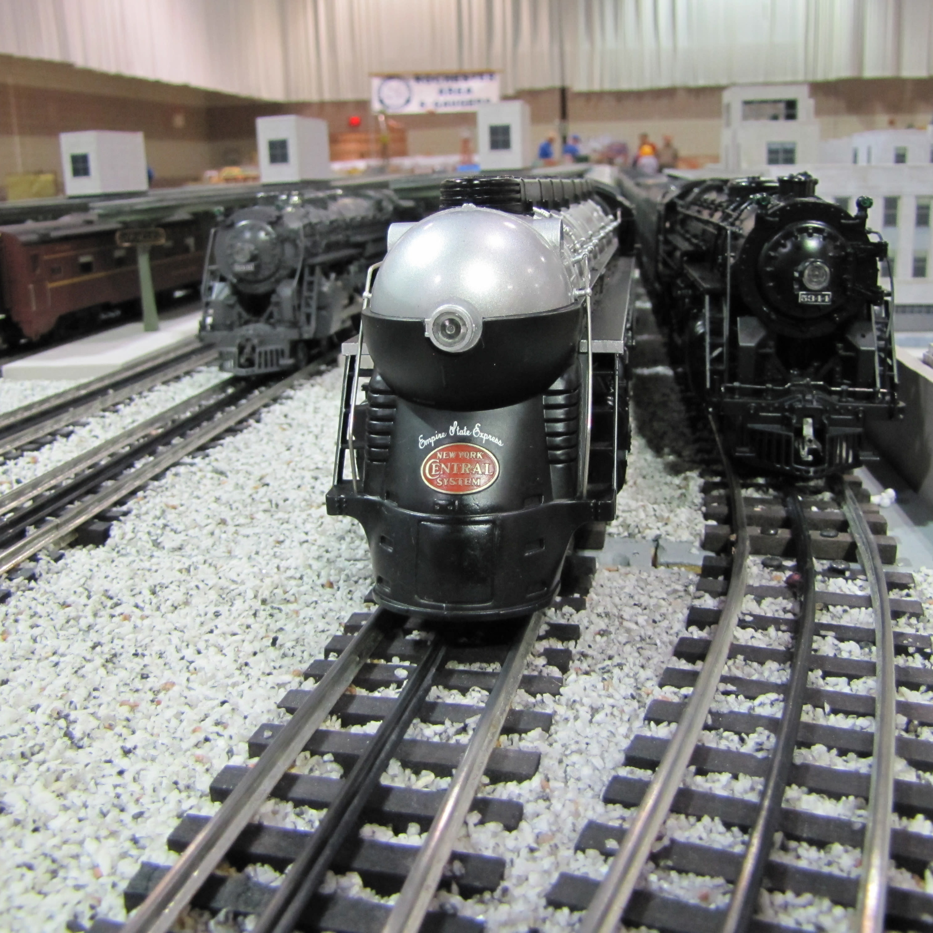 Model trains on display, featuring a sleek silver "Empire State Express" locomotive flanked by two classic black steam engines on parallel tracks