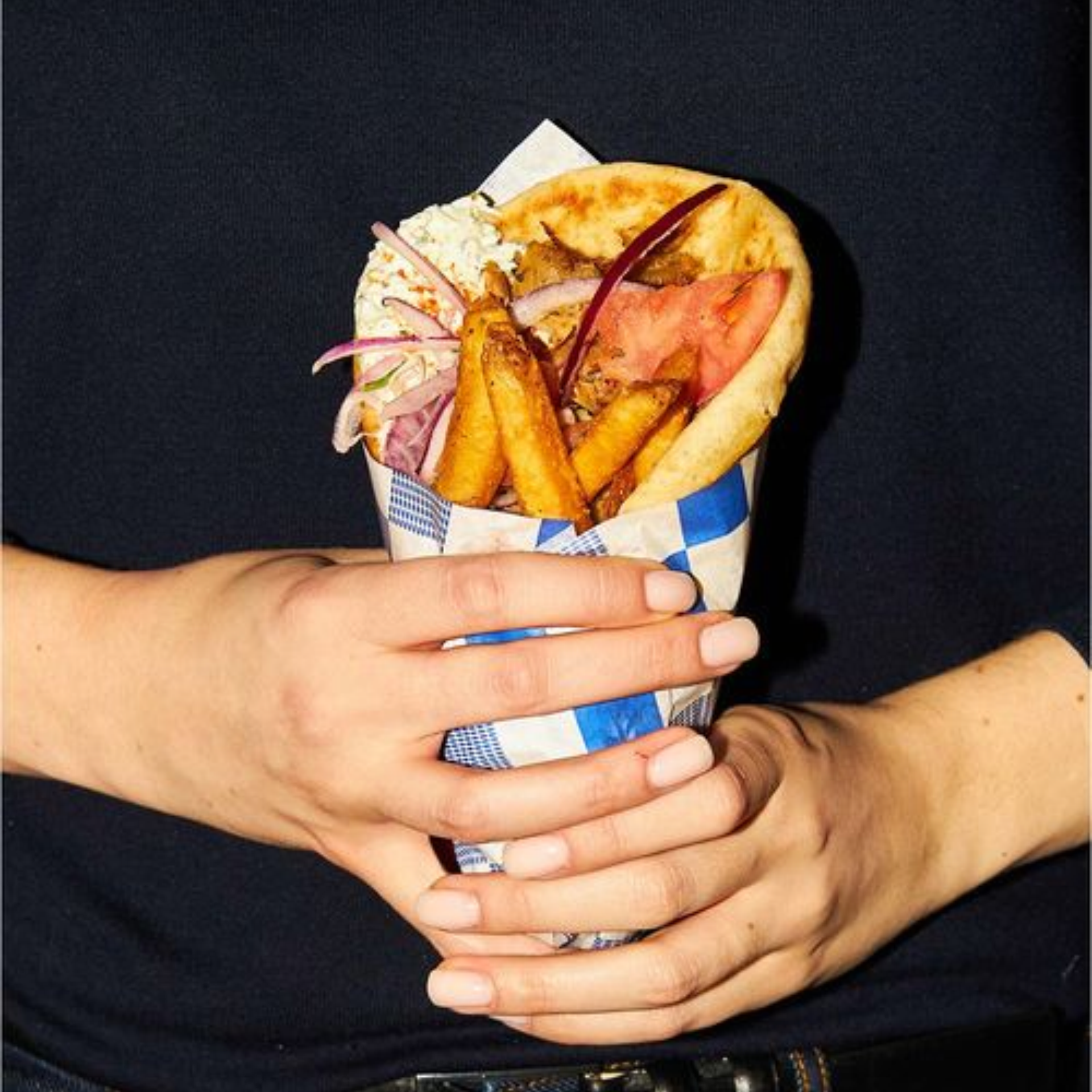 Hand holding gyro wrap with meat, fries, and tzatziki