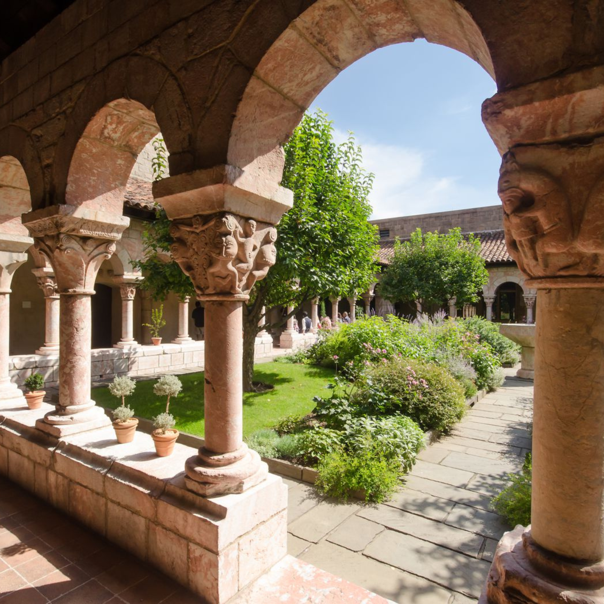 November in NYC: Romanesque cloister garden with carved stone arches, lush greenery, and terracotta pots bathed in warm afternoon sunlight