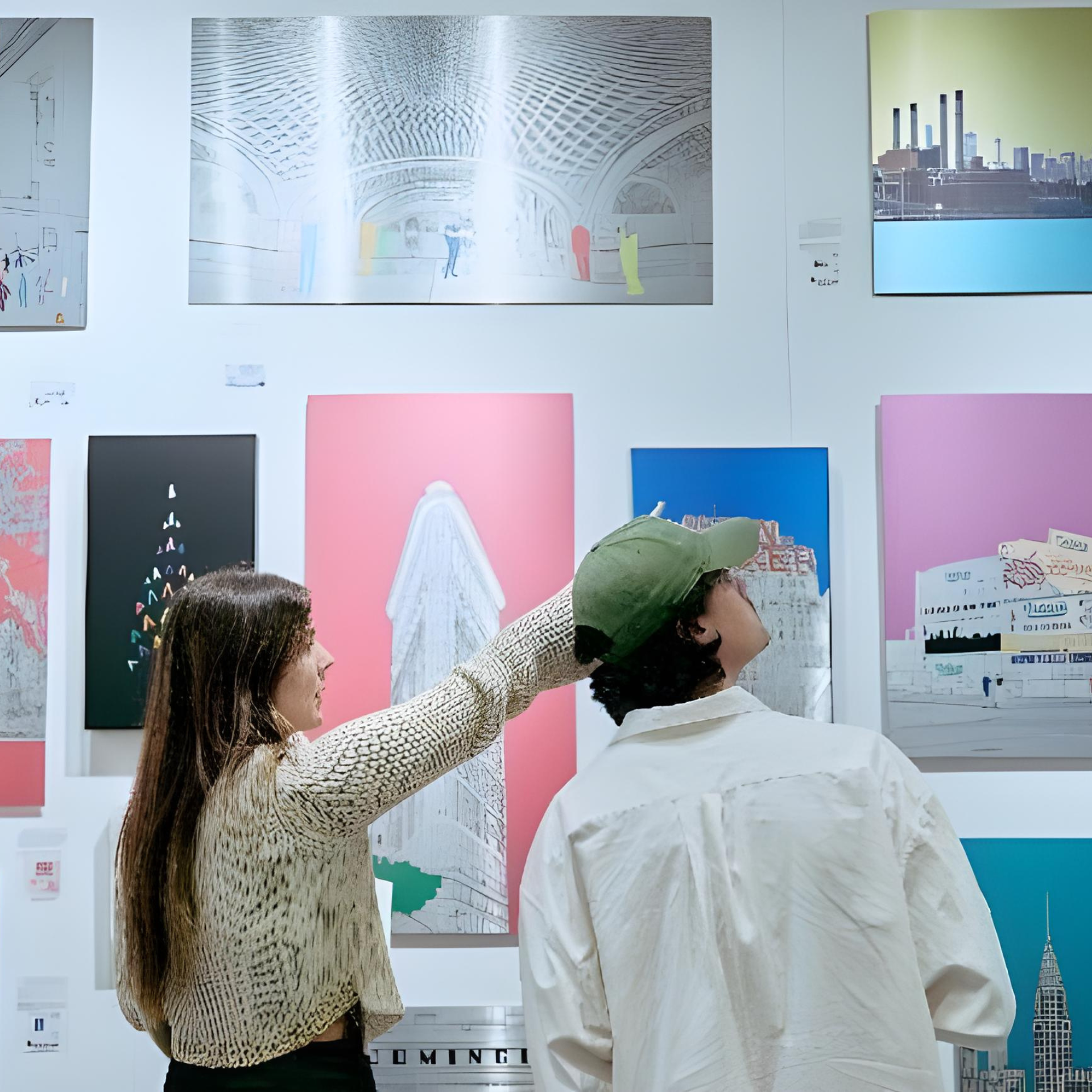Two people view and discuss colorful modern artwork on display in a gallery, with one pointing toward a piece featuring architectural elements