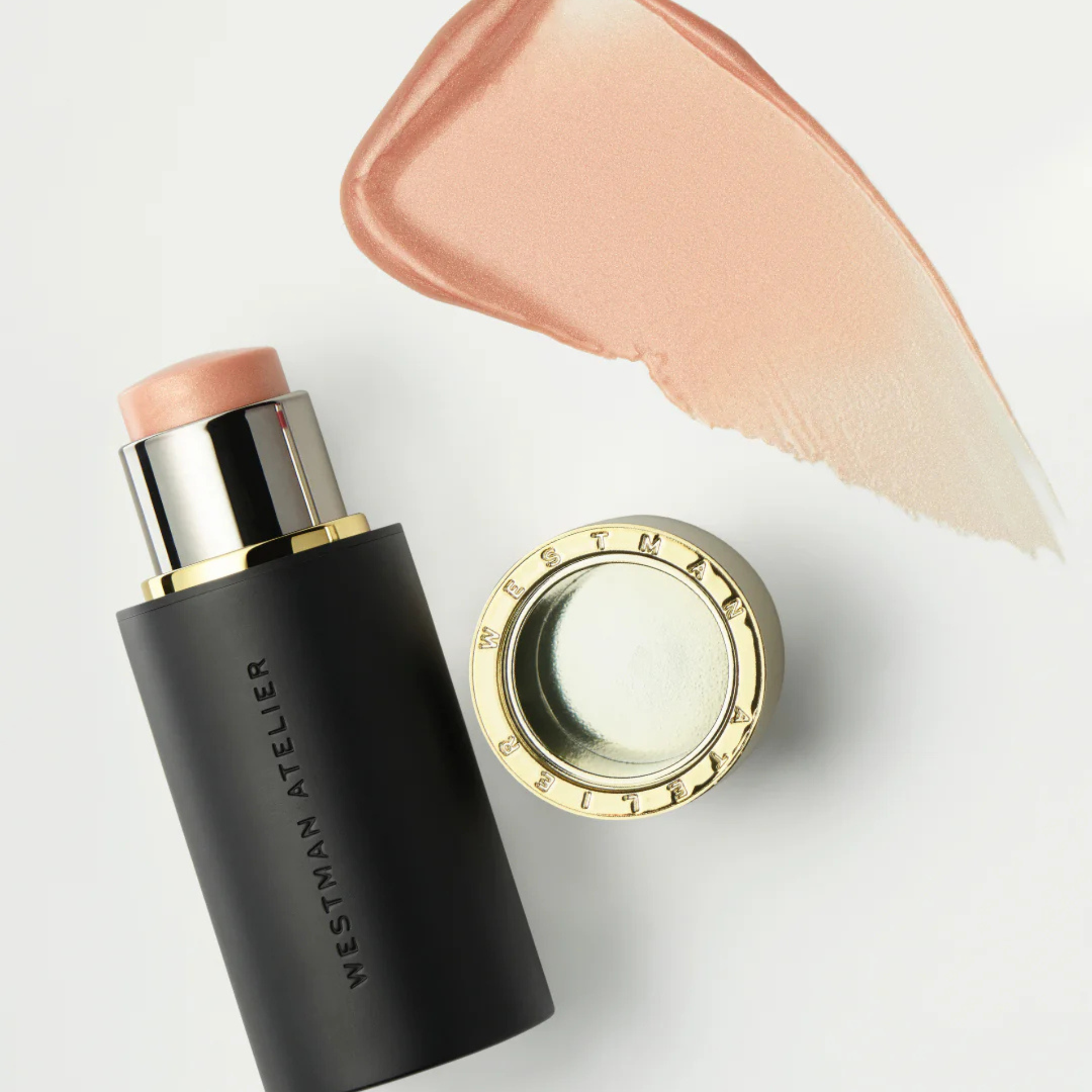 Westman Atelier cream highlighter stick with a peachy-champagne swatch and luxe black-and-gold packaging