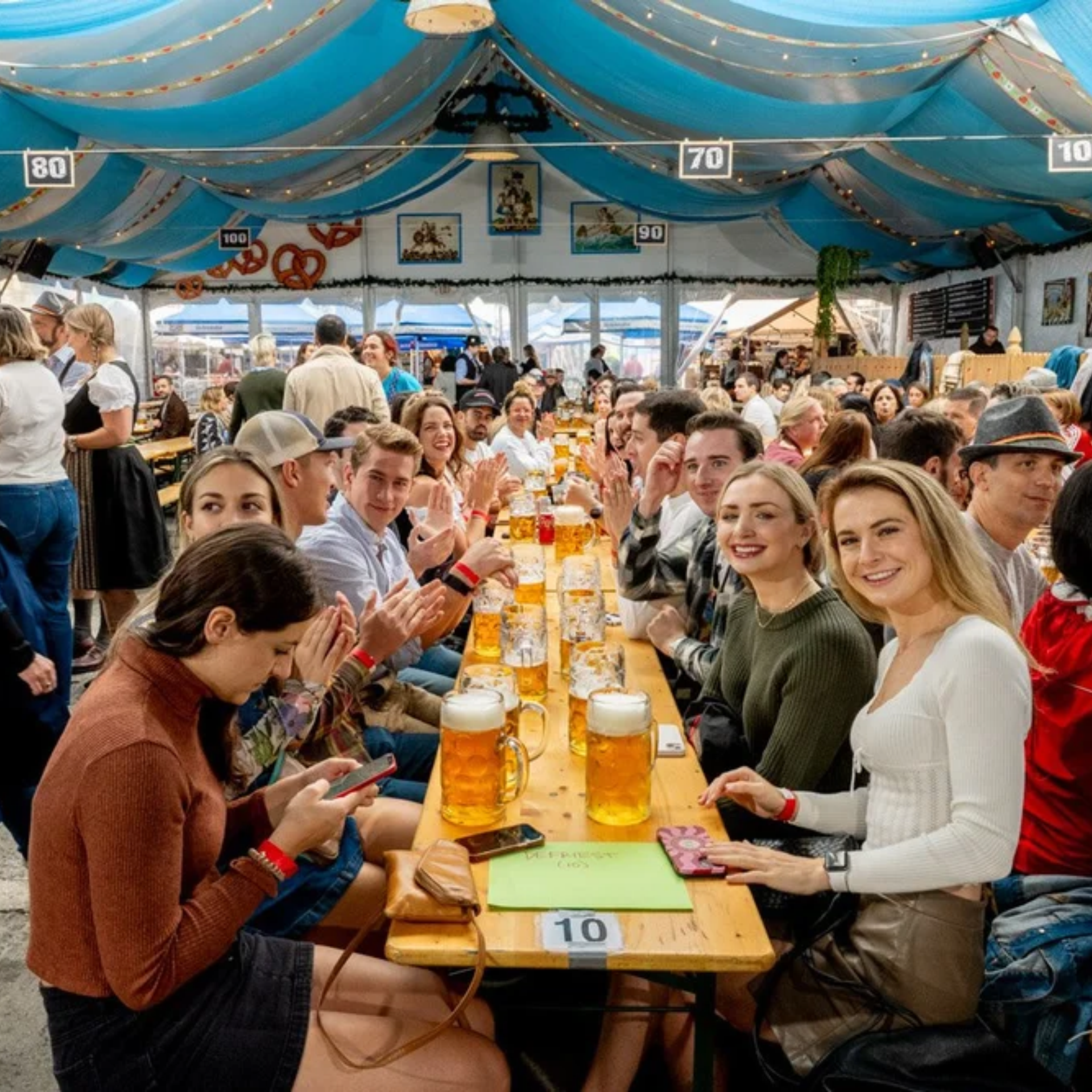 Crowds at long tables with beer mugs under blue‑white drapery