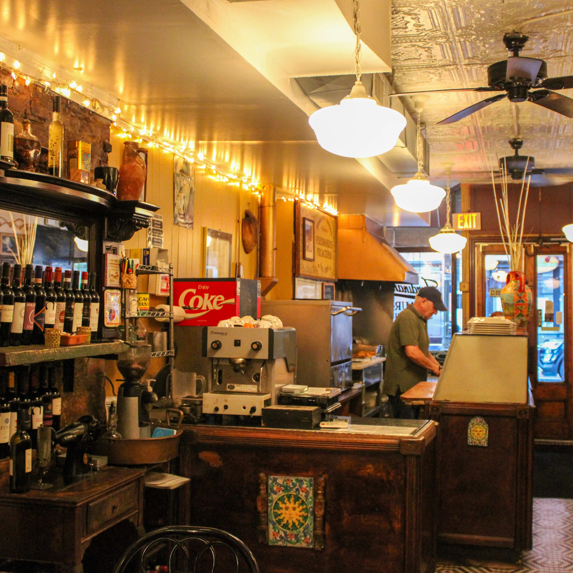 Here are a few simple alt text options for the cozy café interior:
☕ Simple Alt Text Options
- Vintage-style café with warm lighting, rustic decor, and a man working behind the counter